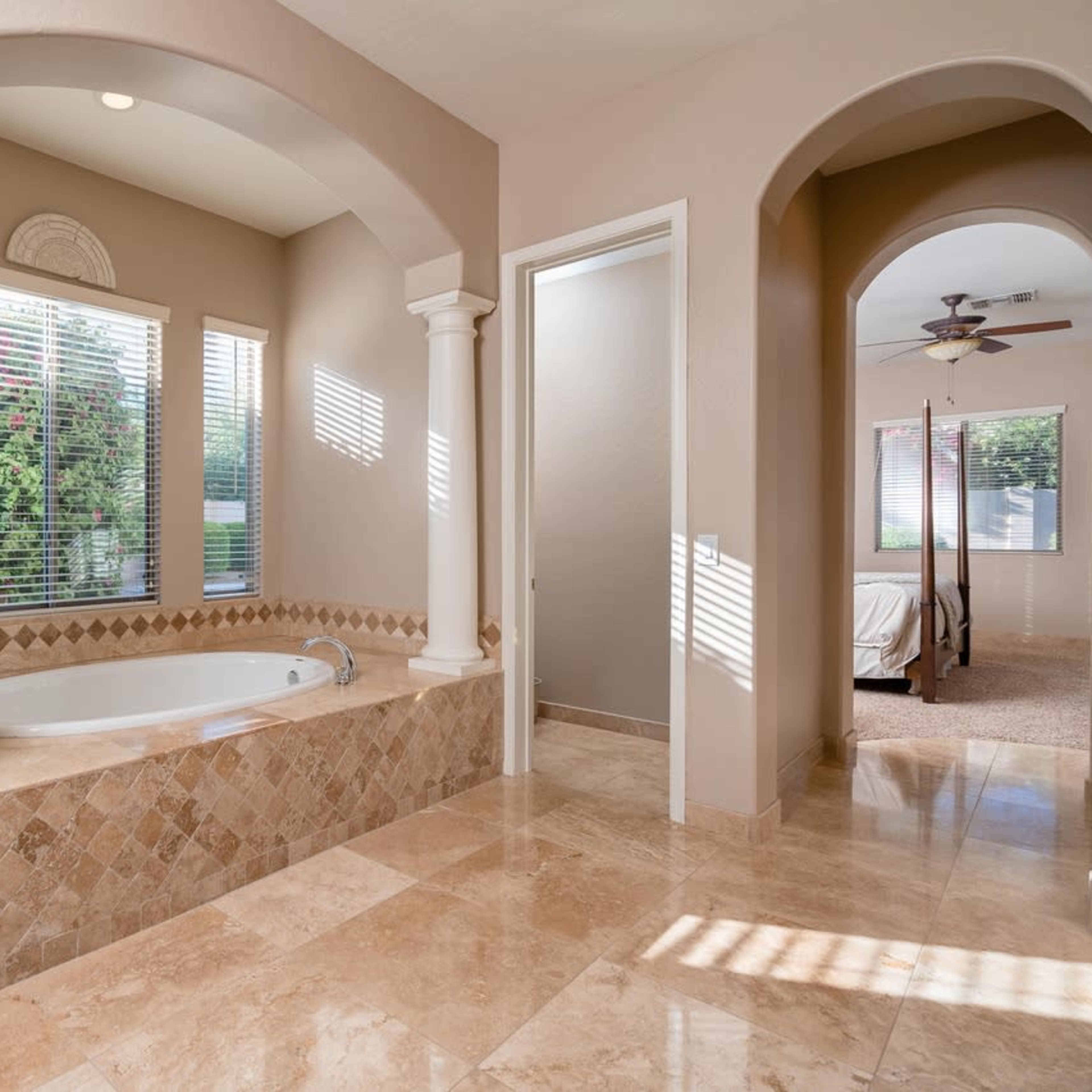 A spacious bathroom featuring a jacuzzi tub, a glass-enclosed shower, and light-colored marble flooring.