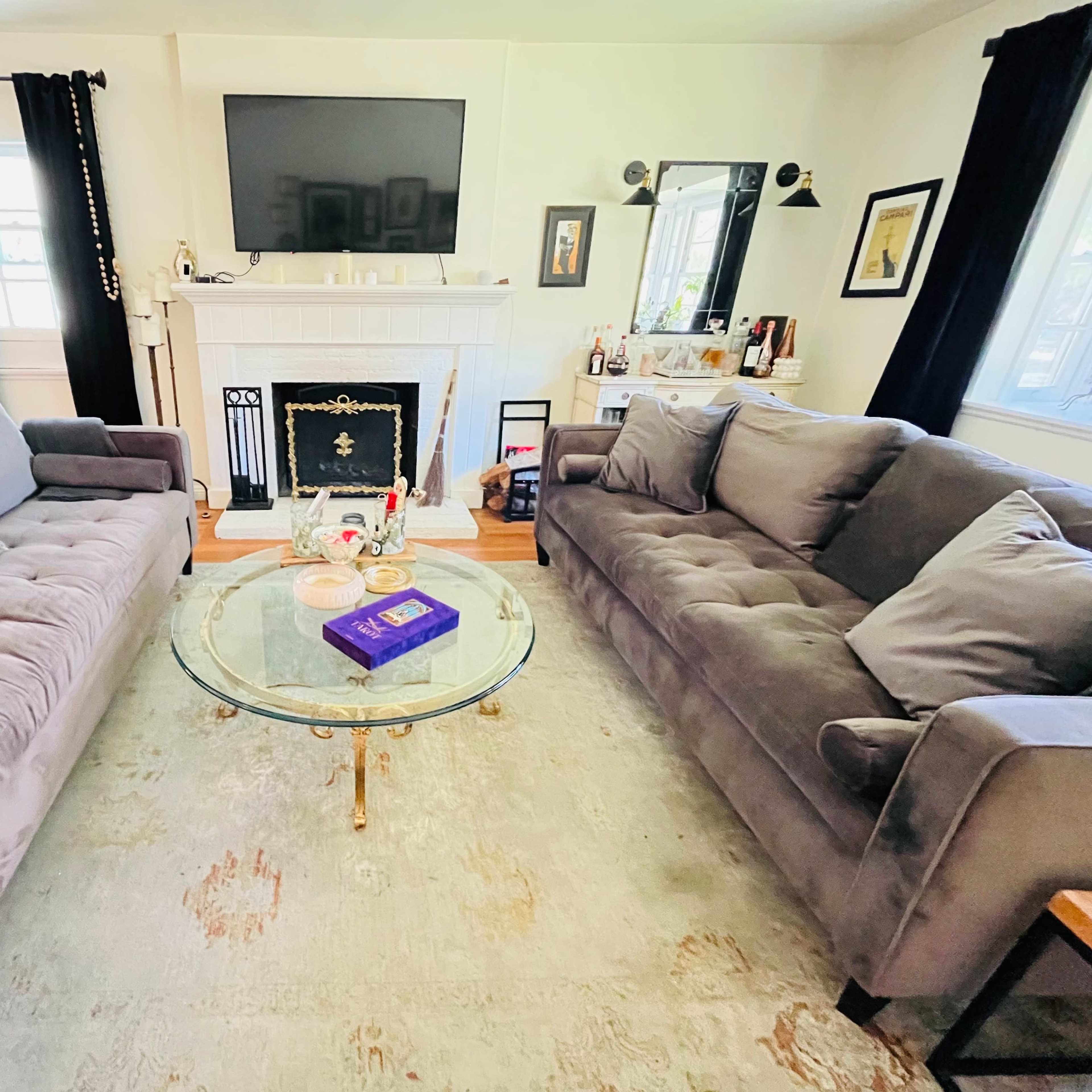 A living room with two gray sofas facing a glass coffee table and a fireplace, and a television mounted on the wall.