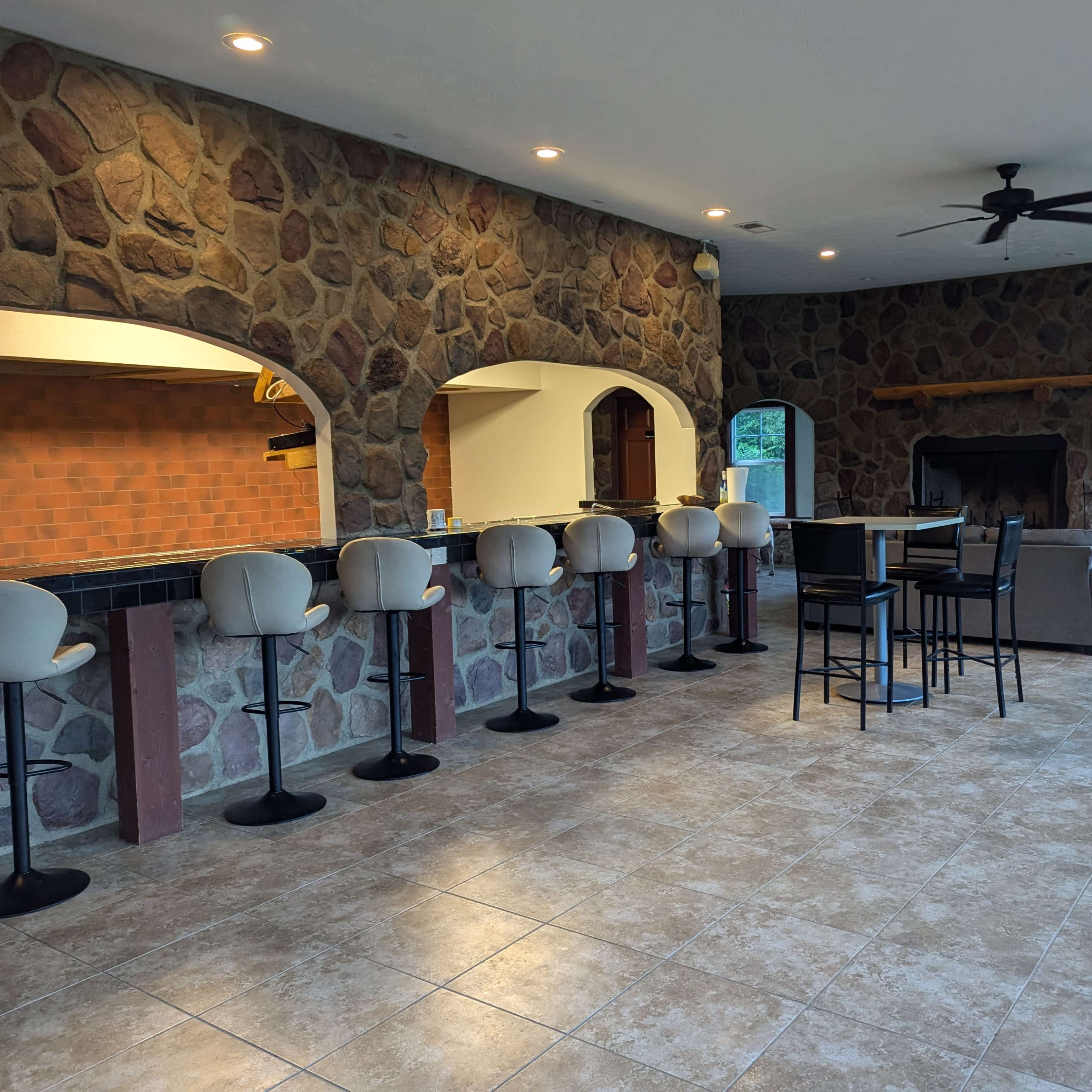 A spacious interior with a stone wall, a bar area with several stools, and a seating arrangement near a fireplace.