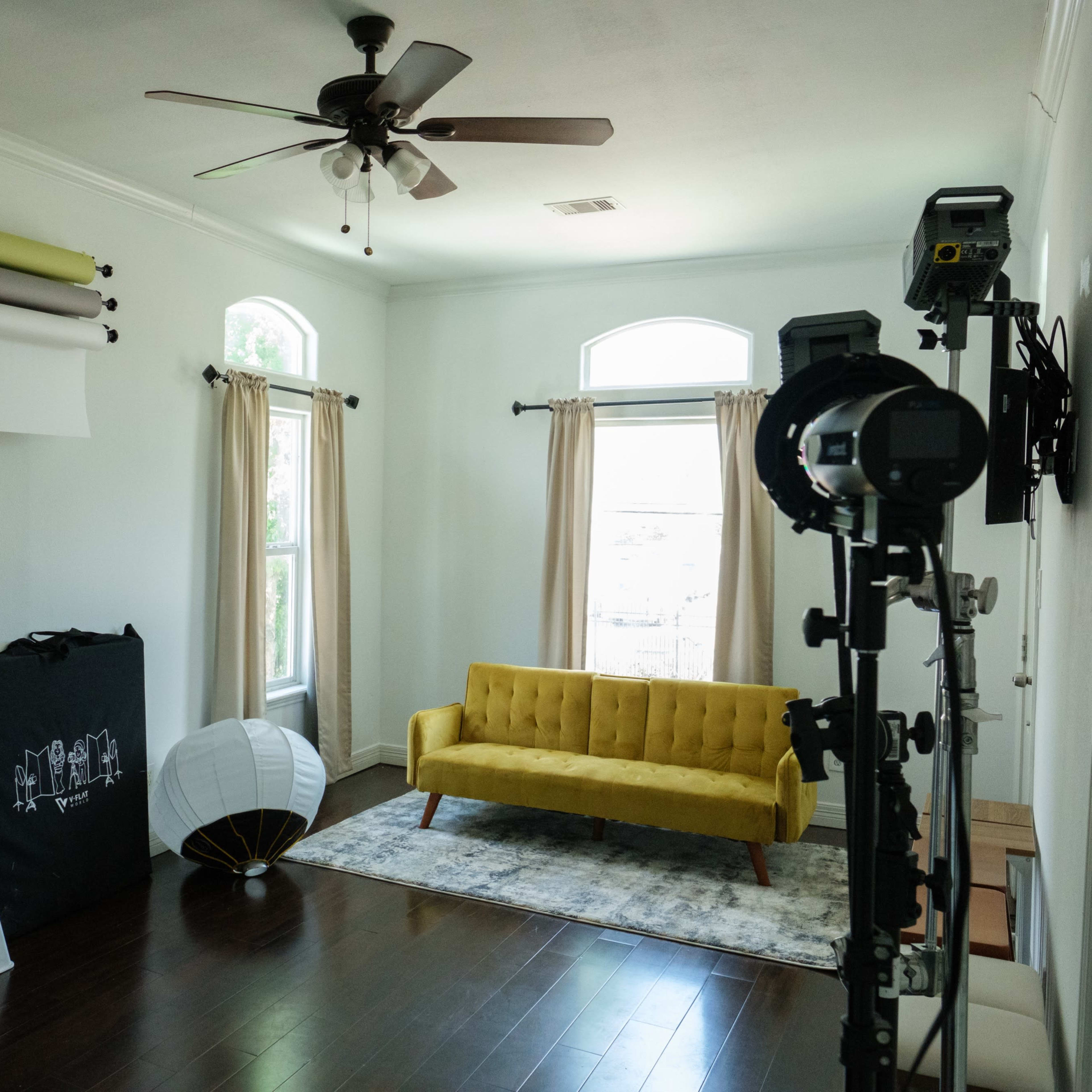 A well-lit room features a yellow couch, a decorative lamp, and photography equipment against the walls.
