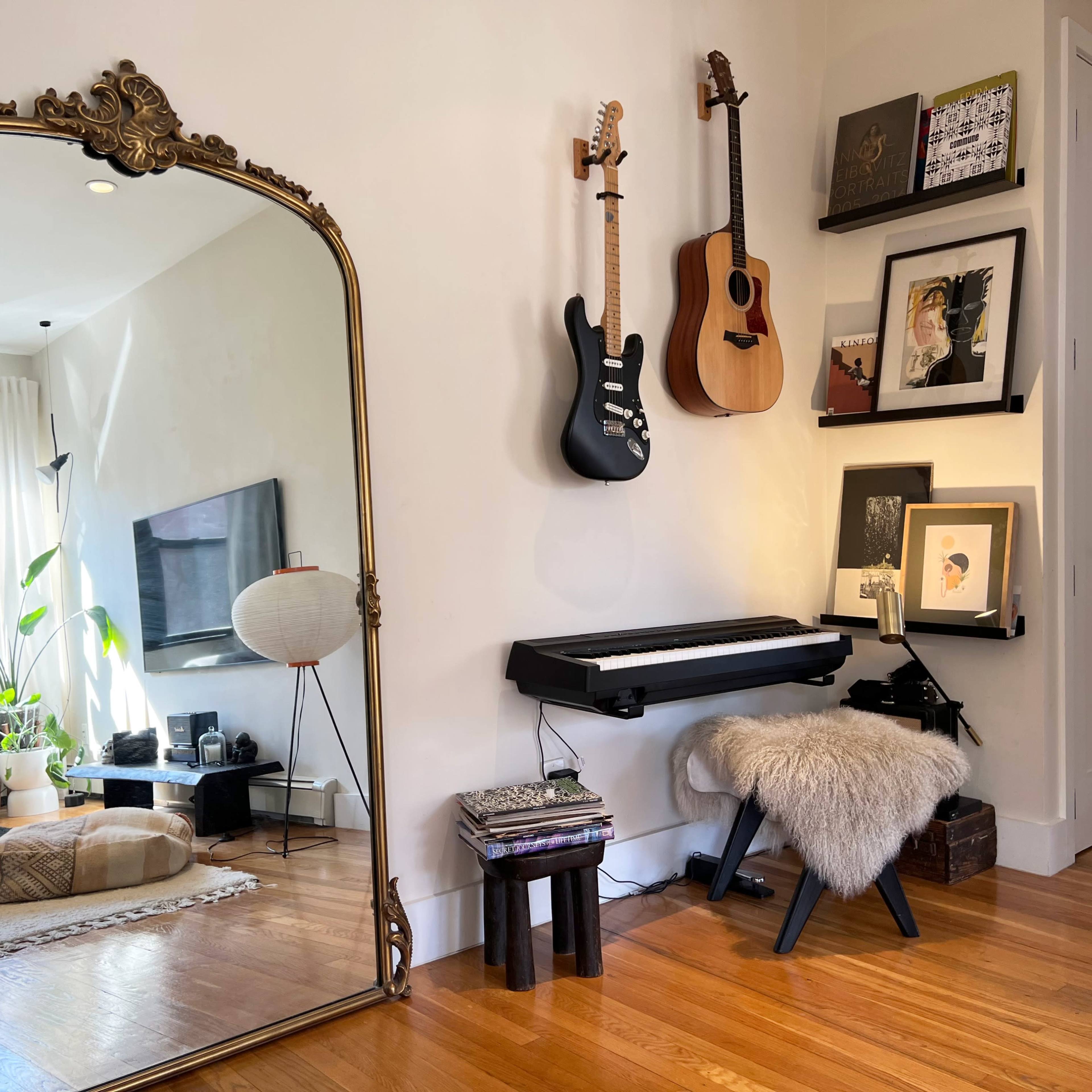 A large ornate mirror reflects a living space with a television, plants, and a cozy seating area, while guitars hang on the wall above a keyboard and decorated shelves.