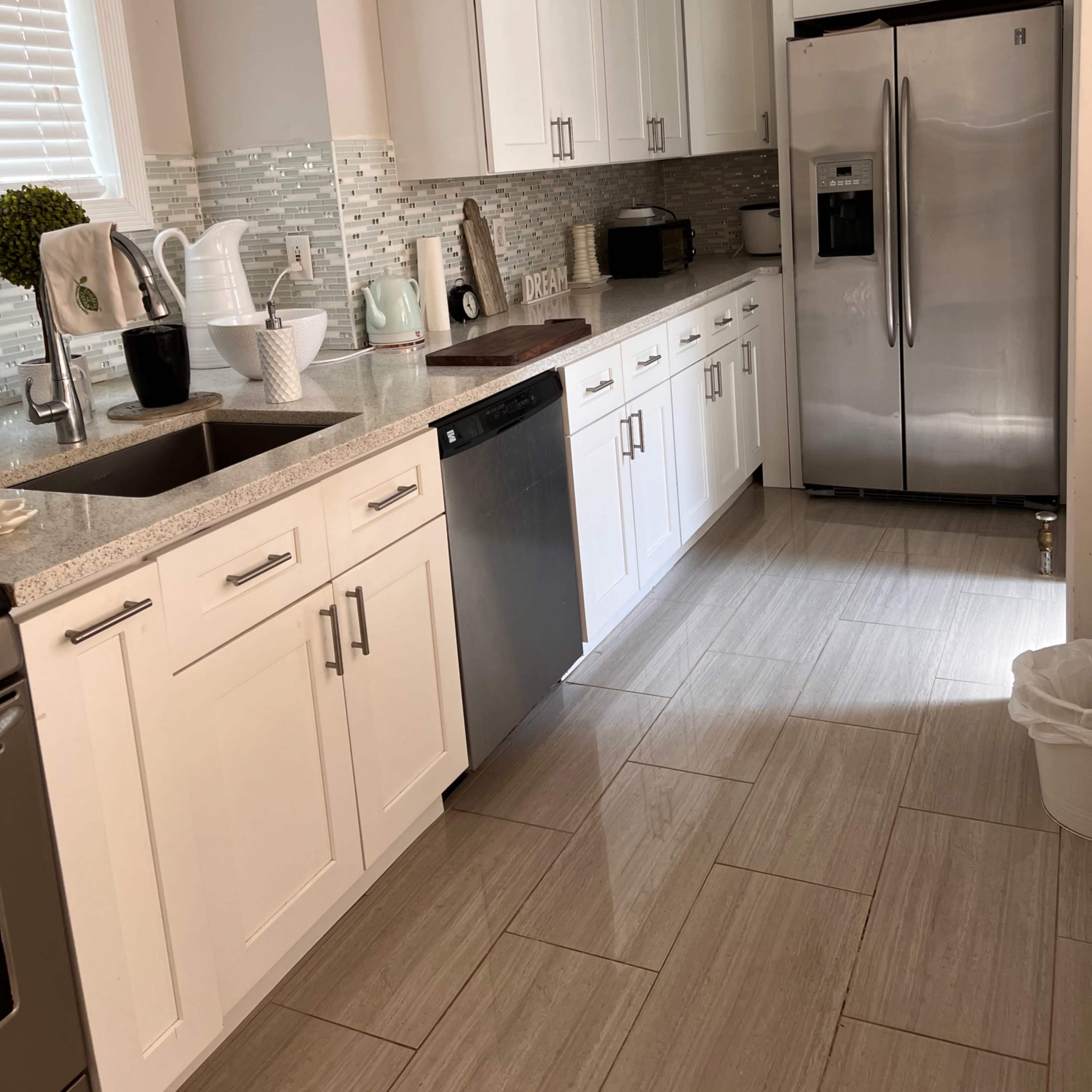 A modern kitchen features white cabinets, a stainless steel refrigerator, and a tiled backsplash.