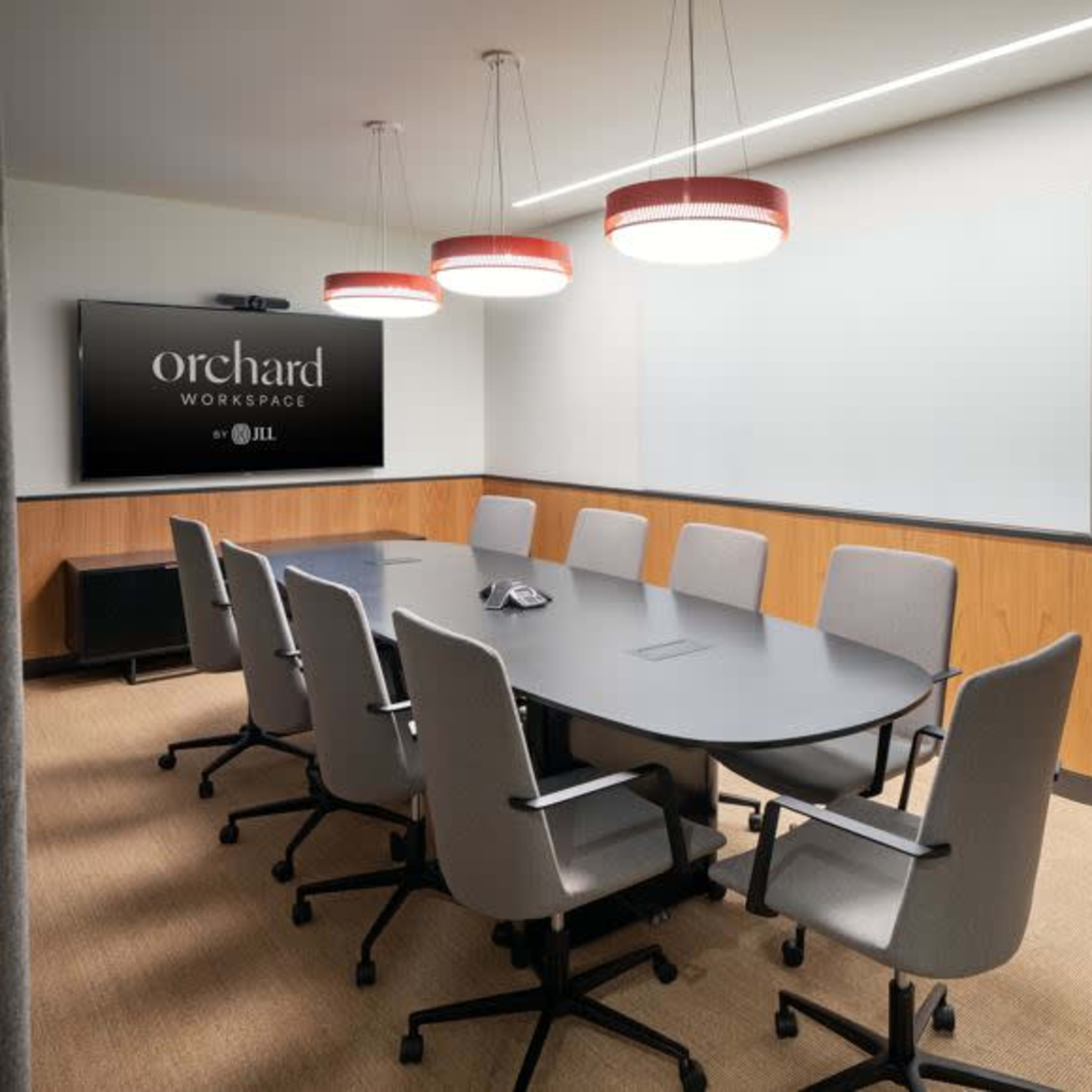 A modern conference room featuring a large oval table surrounded by gray chairs, with a wall-mounted screen and pendant lights above.