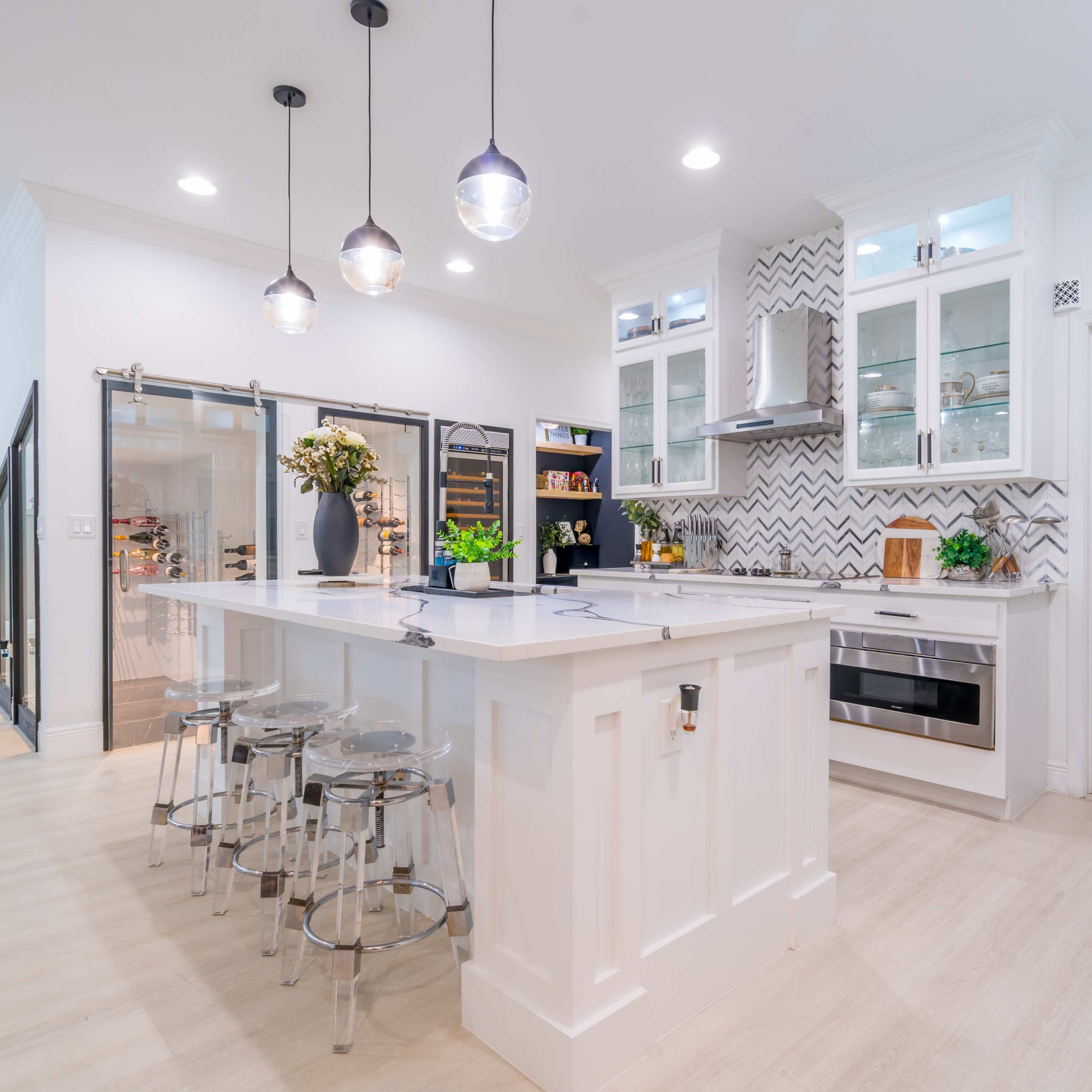 A modern kitchen features an island with bar stools, sleek cabinetry, and pendant lighting above.