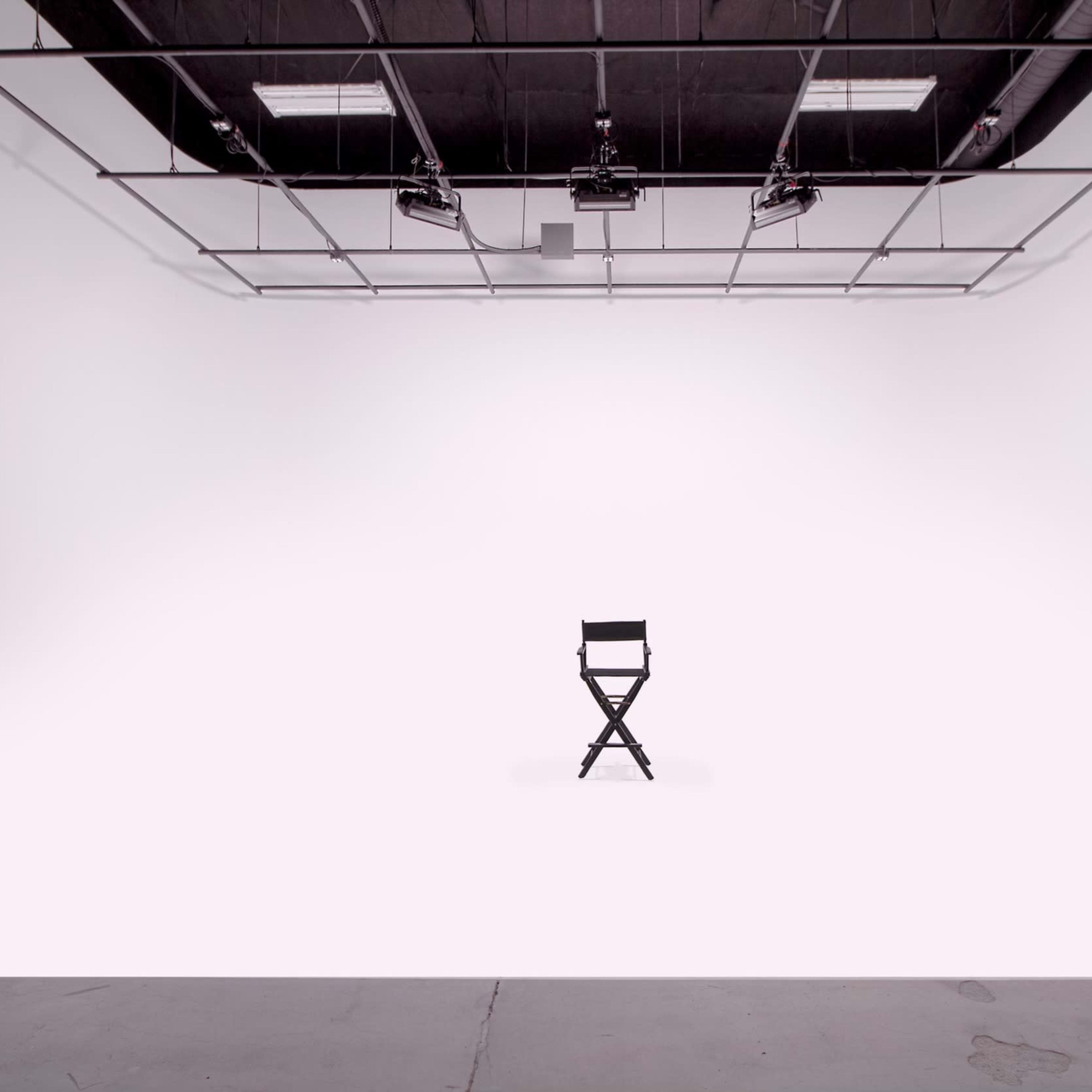 A single black director's chair is positioned in the center of a spacious, empty white studio.
