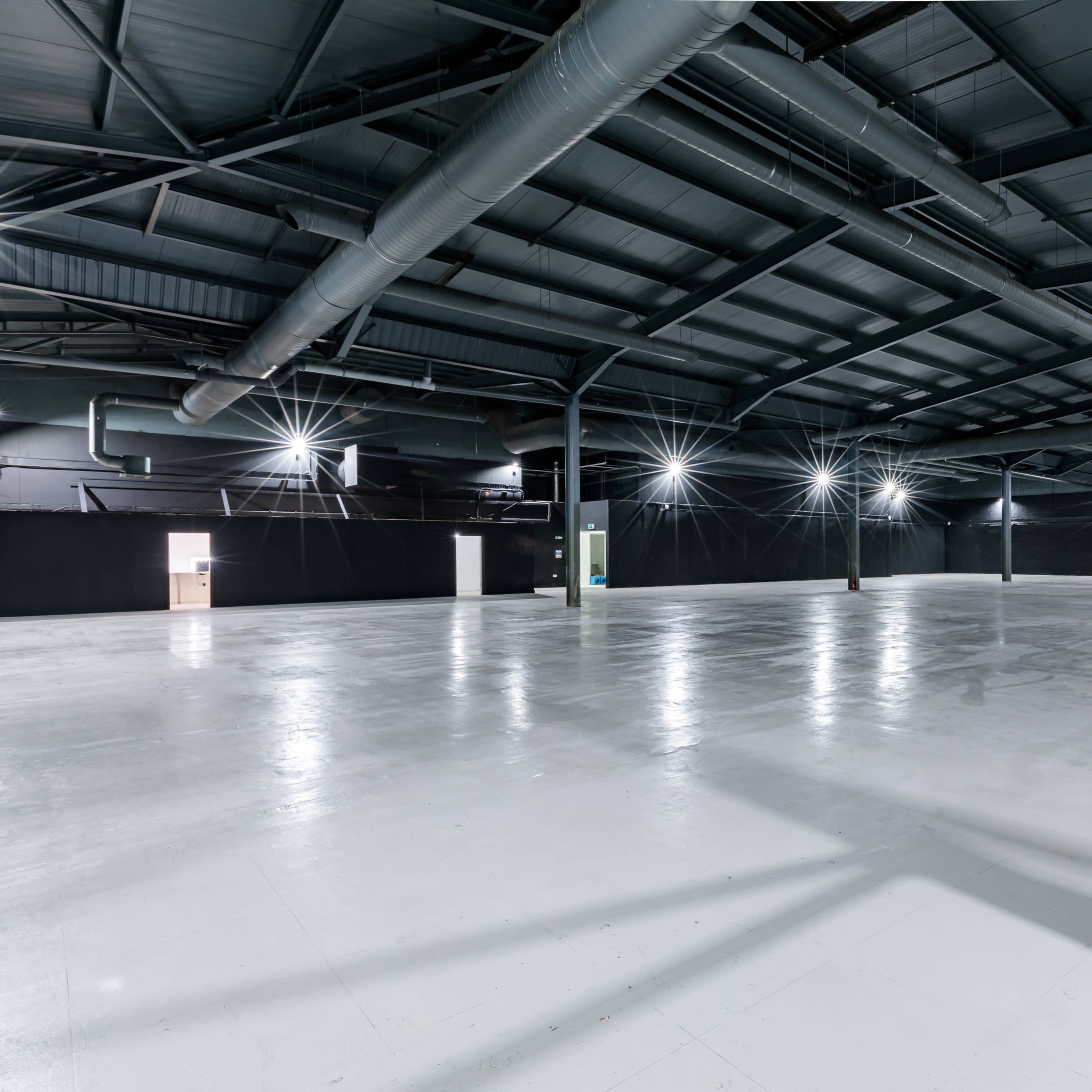 A large, empty industrial space with a high ceiling and overhead lighting.