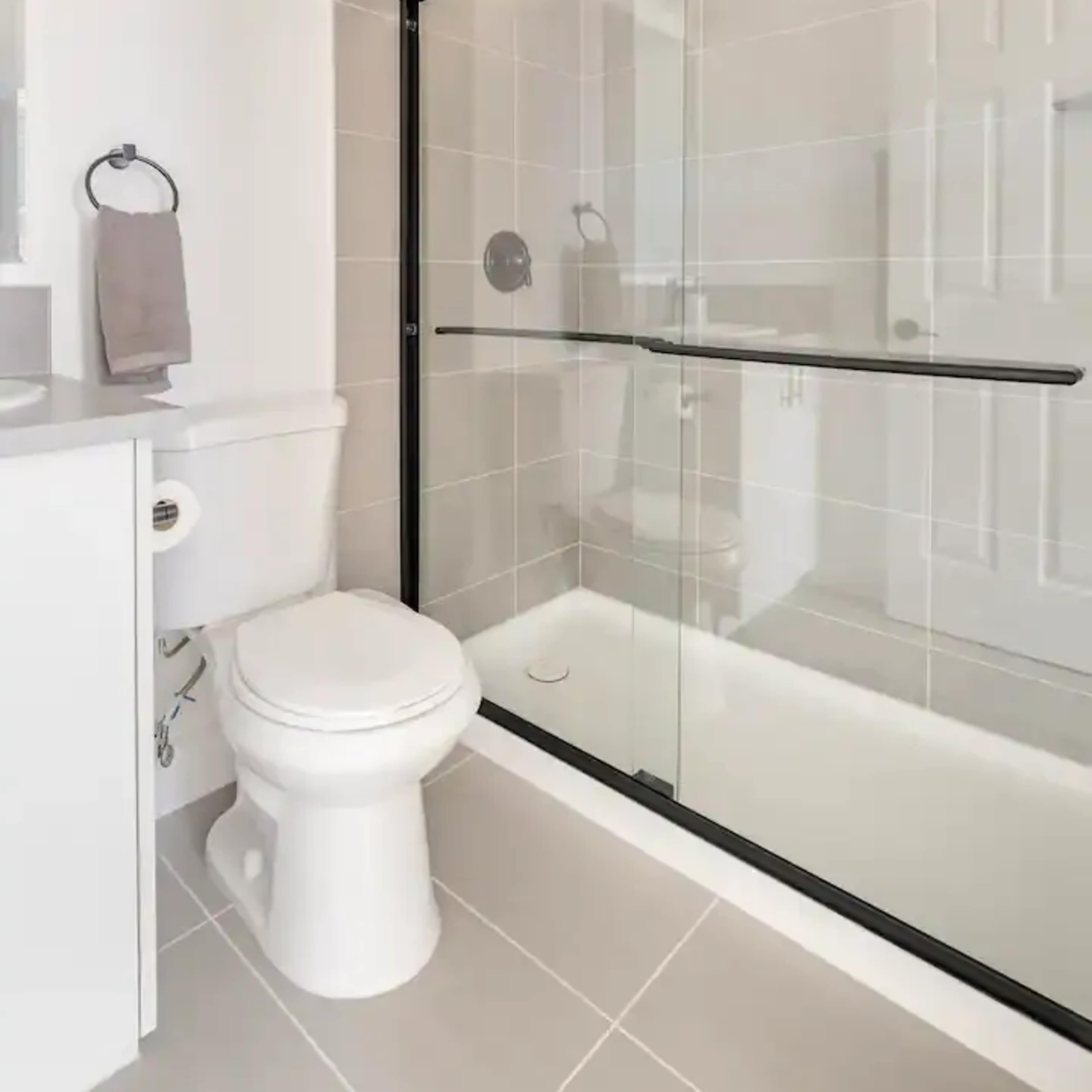 A modern bathroom featuring a glass shower enclosure, a toilet, and neutral tiled walls.