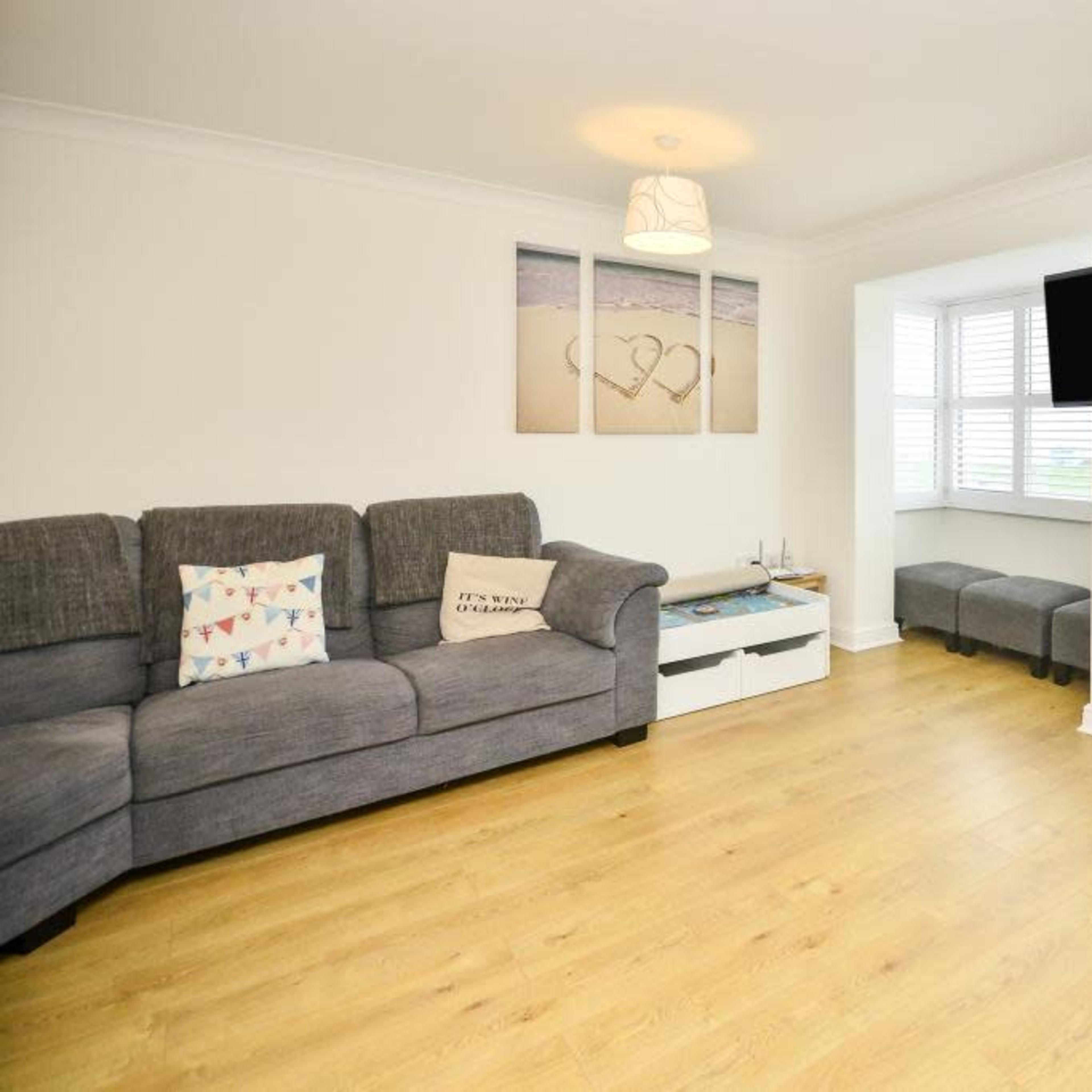 A cozy living room with a gray sectional sofa, a coffee table, a TV mounted on the wall, and a door leading to a balcony.