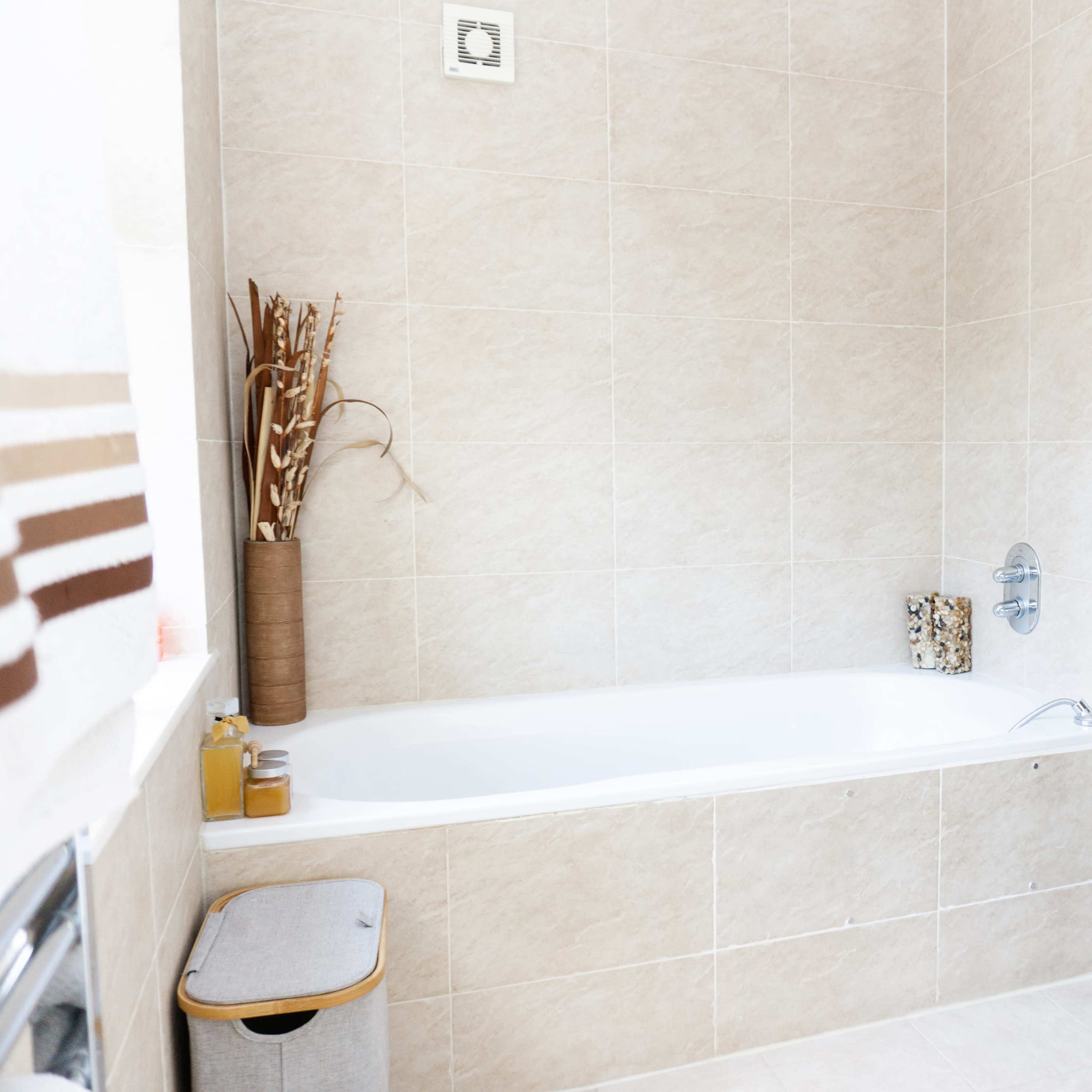 A light-colored tiled bathroom featuring a bathtub, a small storage unit, and a separate shower area.