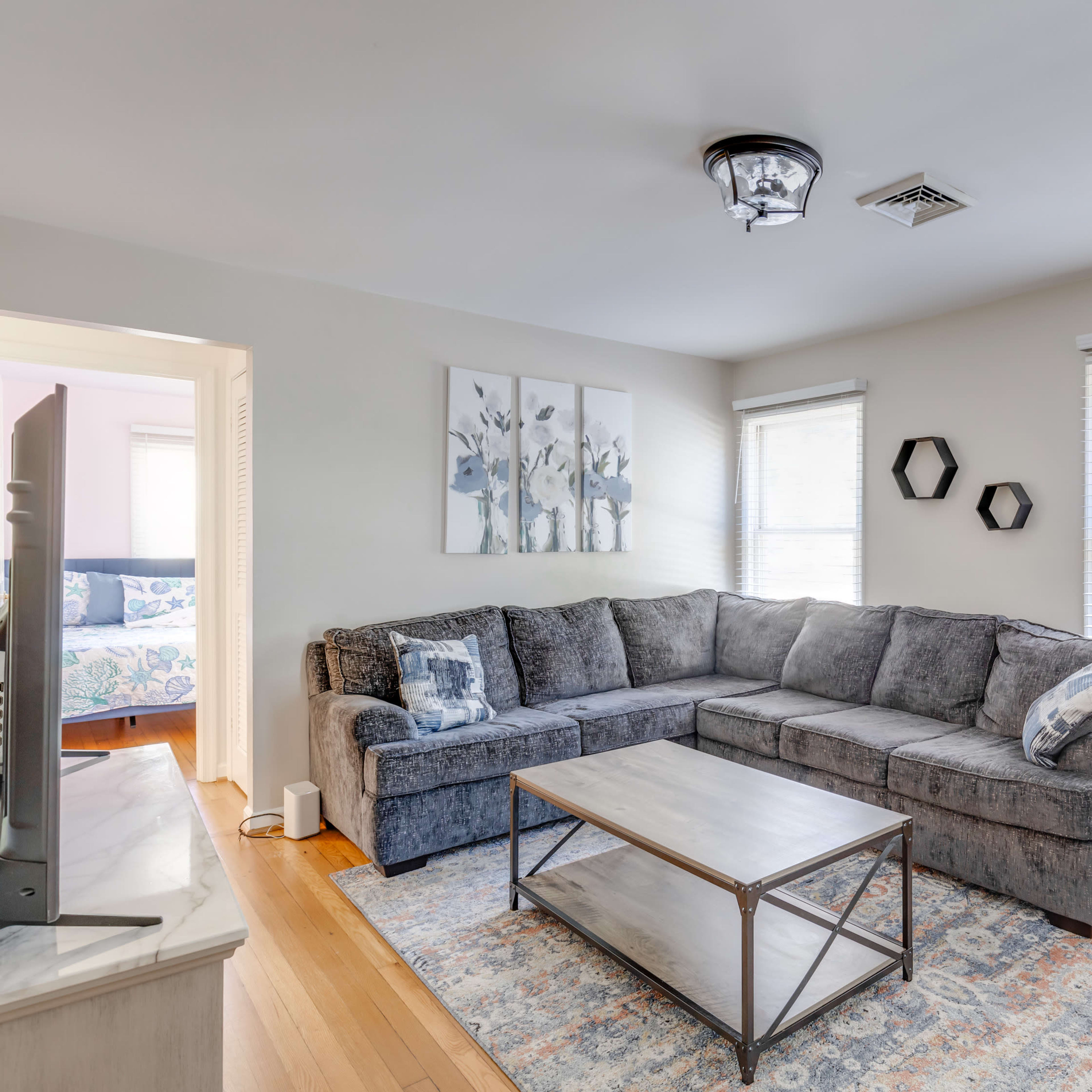 A living room featuring a gray sectional sofa, a rectangular coffee table, and two windows with white blinds.
