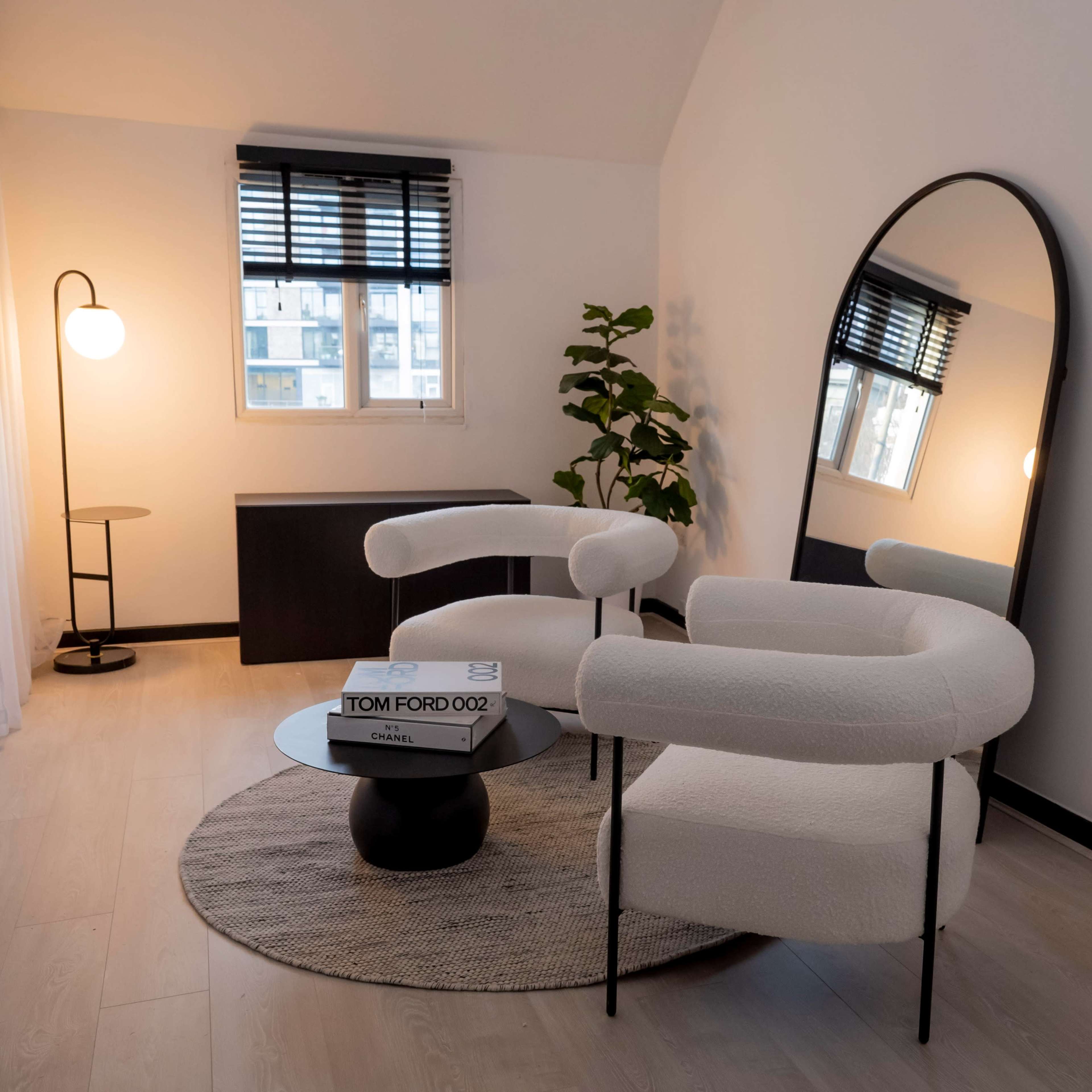 A minimalist living space featuring two round armchairs, a large mirror, a floor lamp, a potted plant, and a coffee table with a book on it.