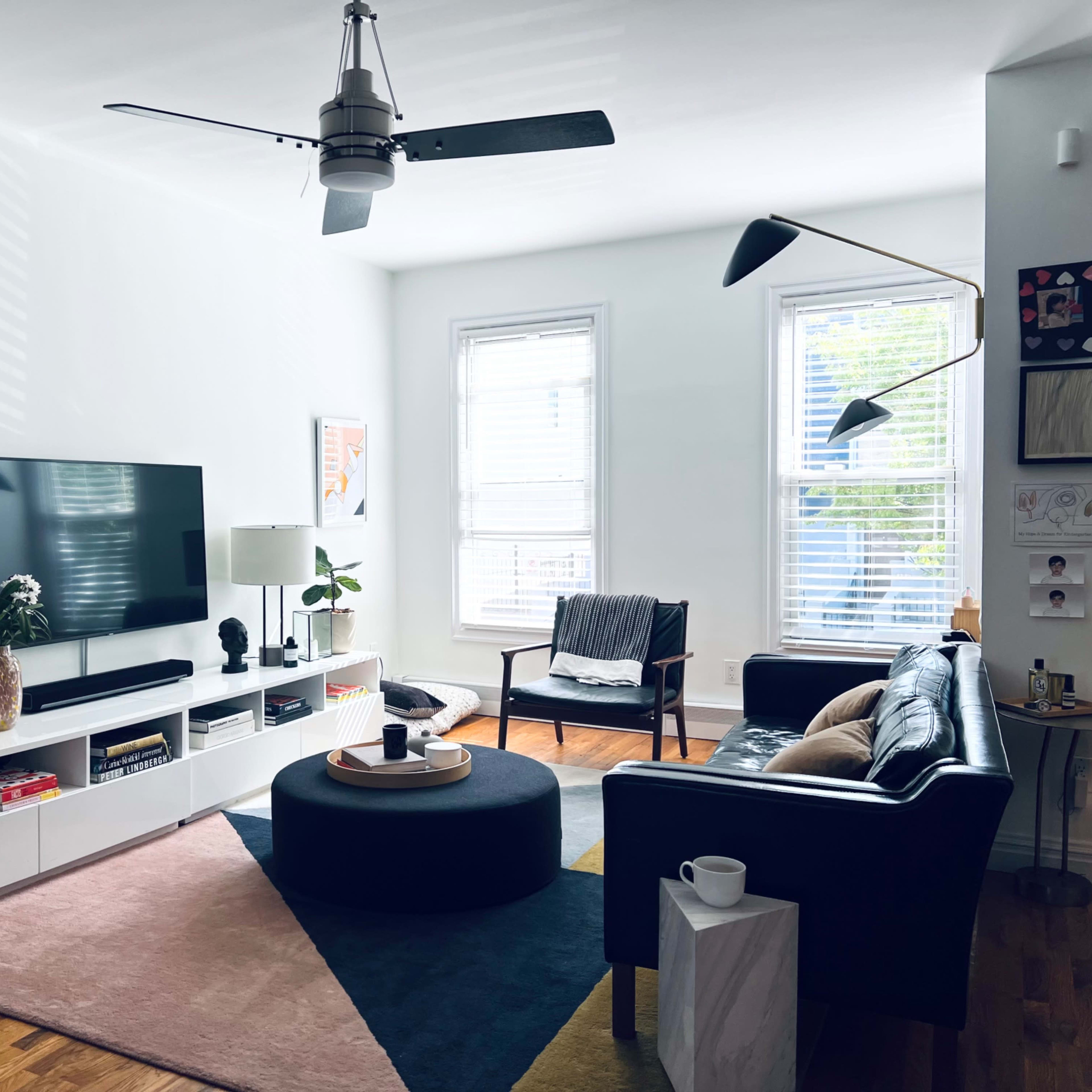 A modern living room featuring a television mounted on the wall, a black leather sofa, a round coffee table, and a bookshelf stacked with books.