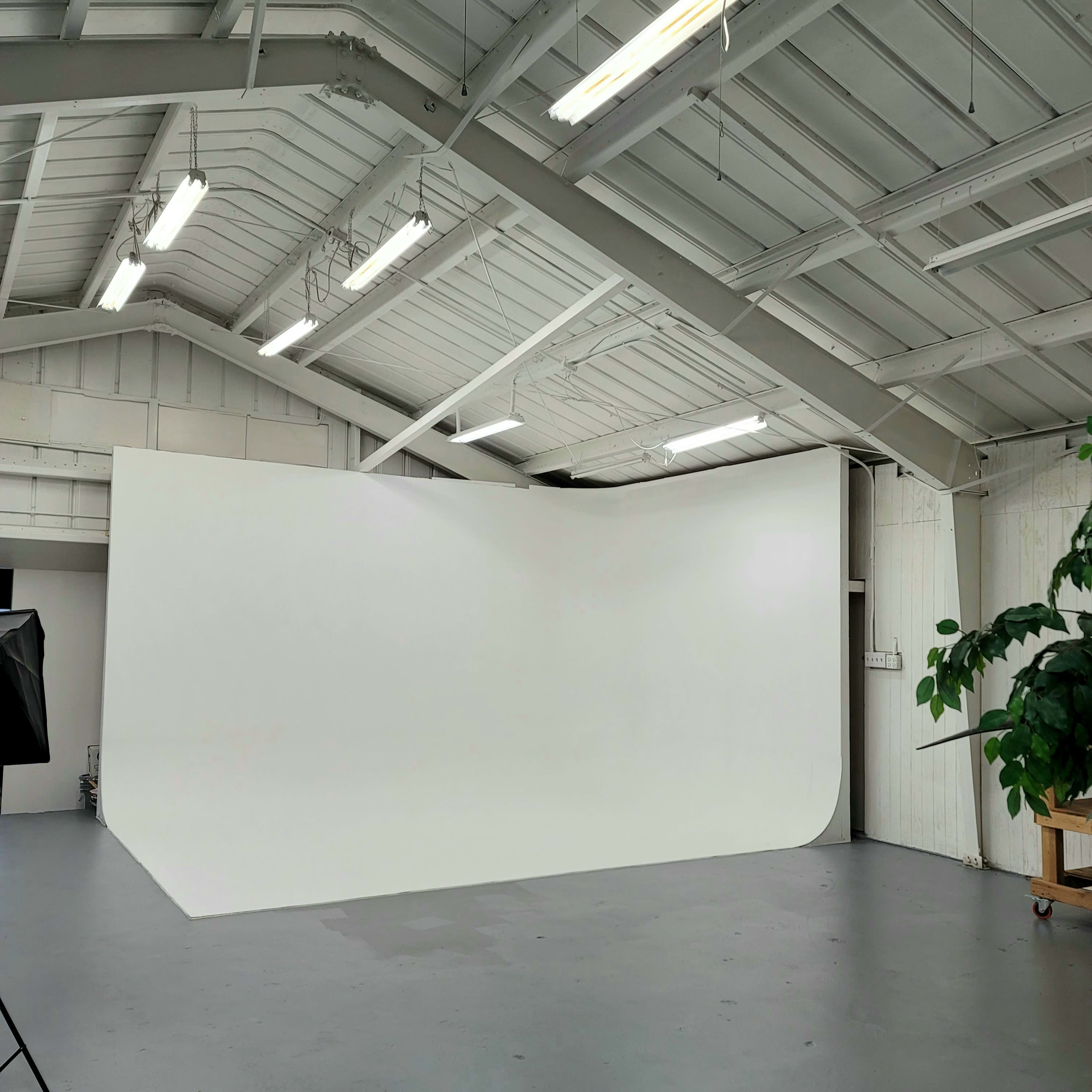 A spacious studio with a large, curved white backdrop and high ceilings, illuminated by overhead lights.