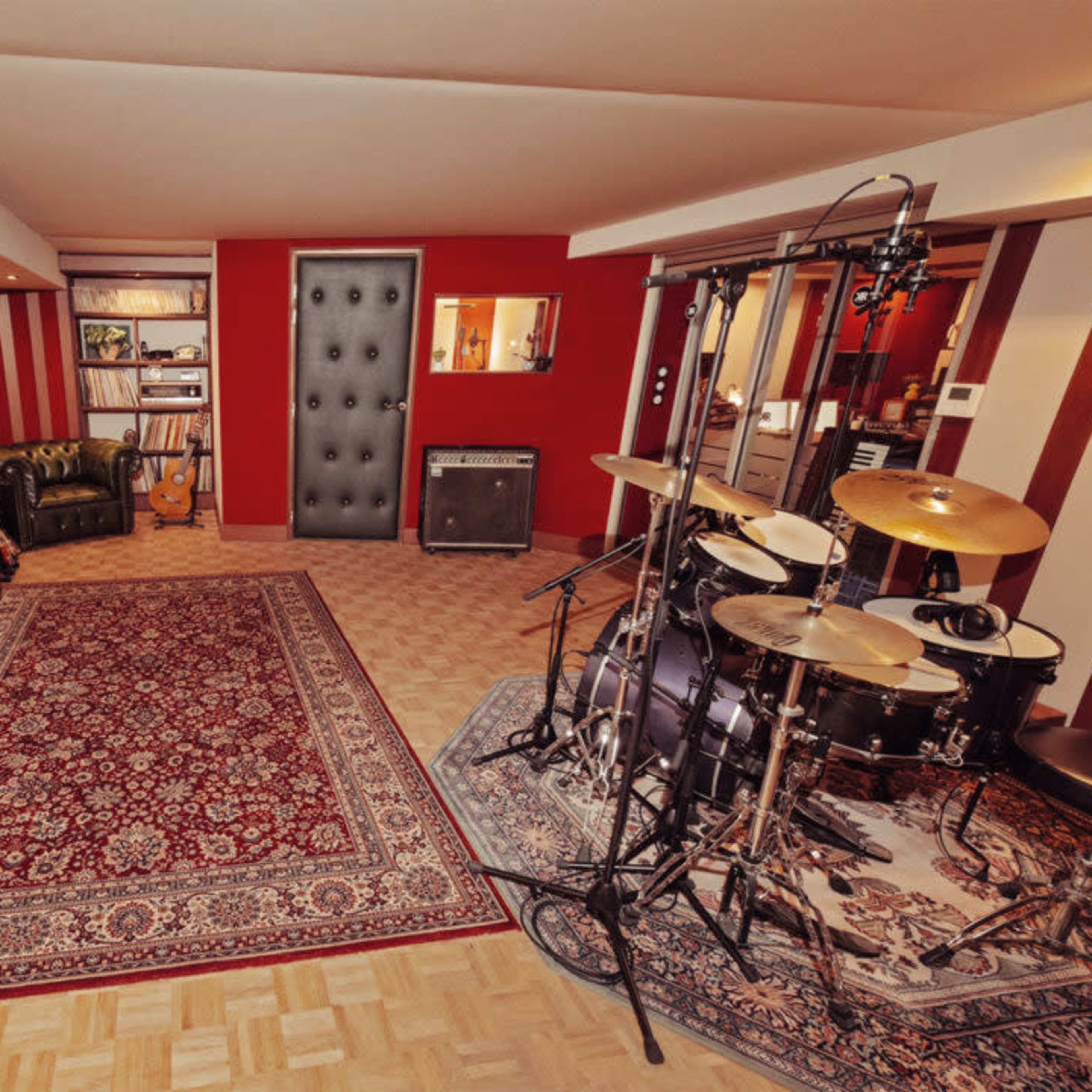 A well-equipped music studio featuring a drum set, a keyboard, a guitar, and a decorative plant, all arranged on a patterned rug.