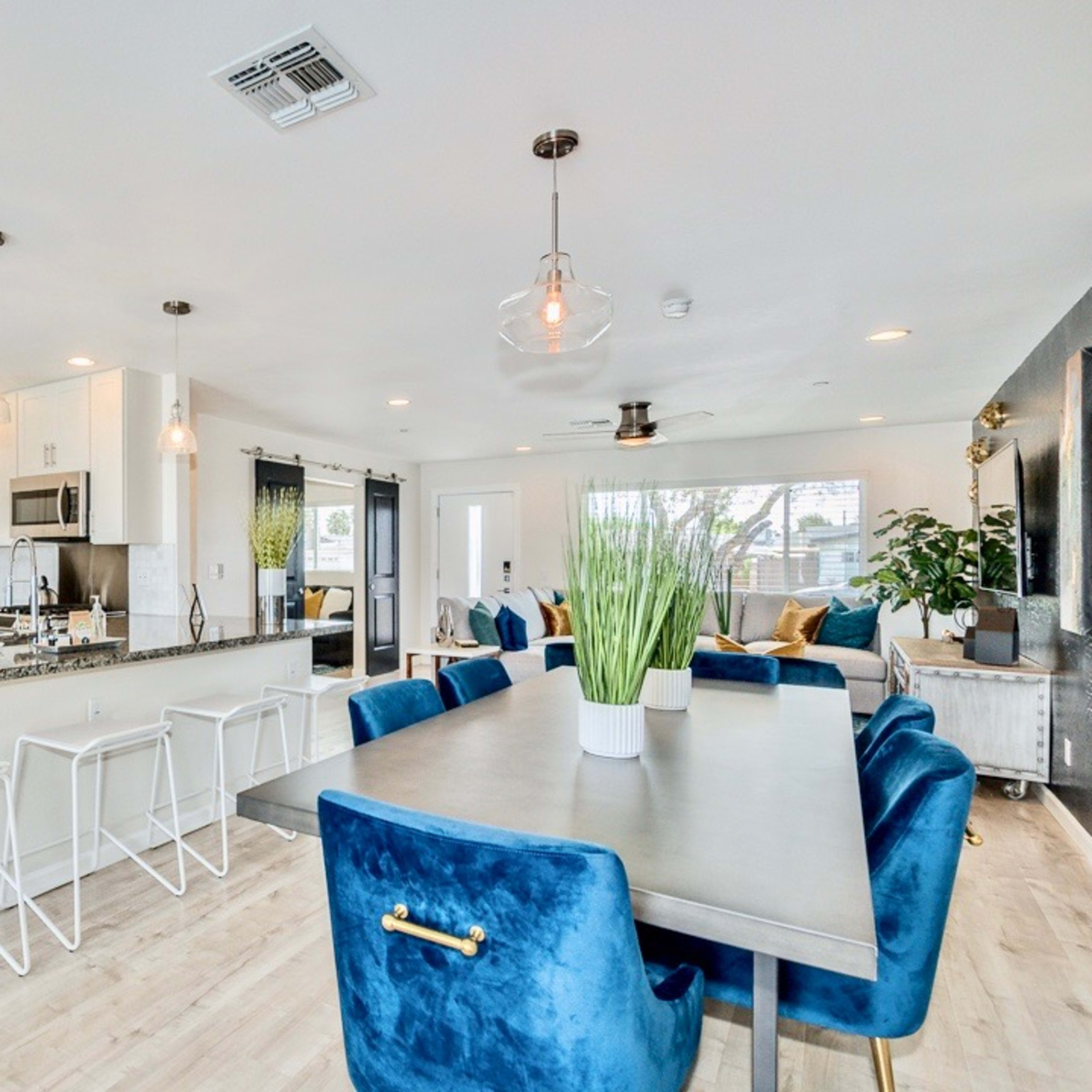 A modern kitchen and dining area features a large table surrounded by blue chairs, with an island bar and stainless steel appliances in a bright, open space.
