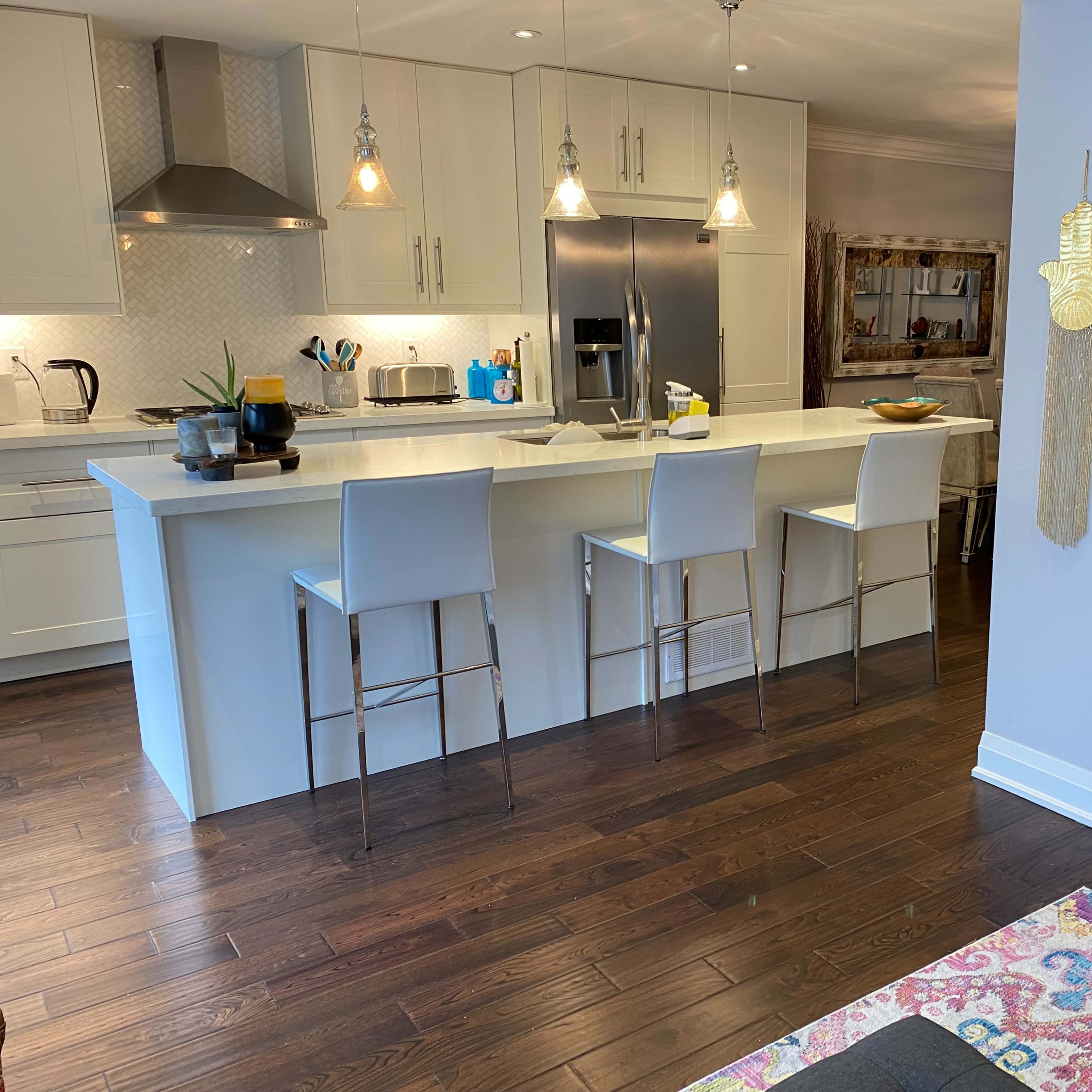 A modern kitchen with white cabinetry, a central island with bar stools, and hardwood flooring.