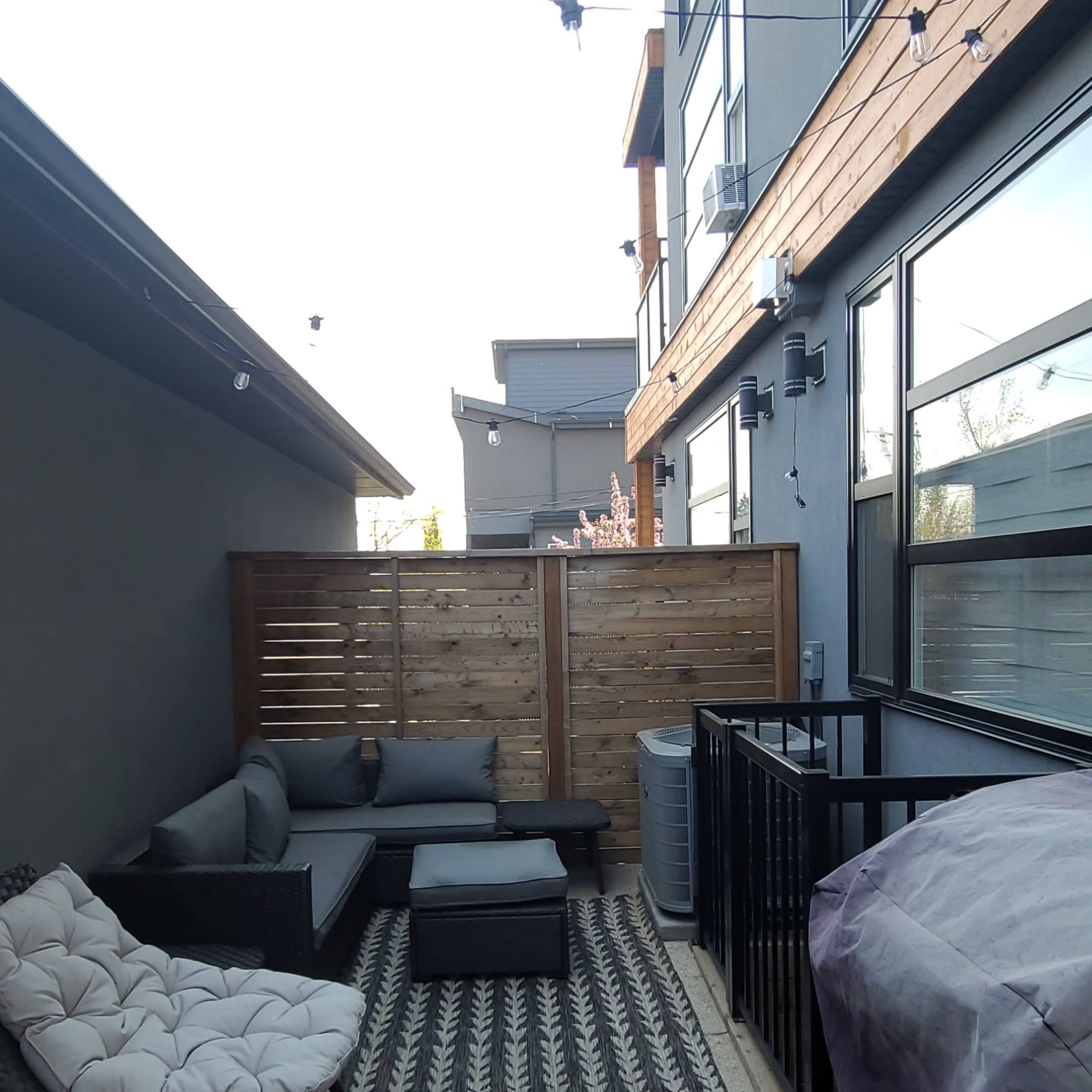 A small outdoor patio area with modern seating, a patterned rug, and wooden privacy screens.