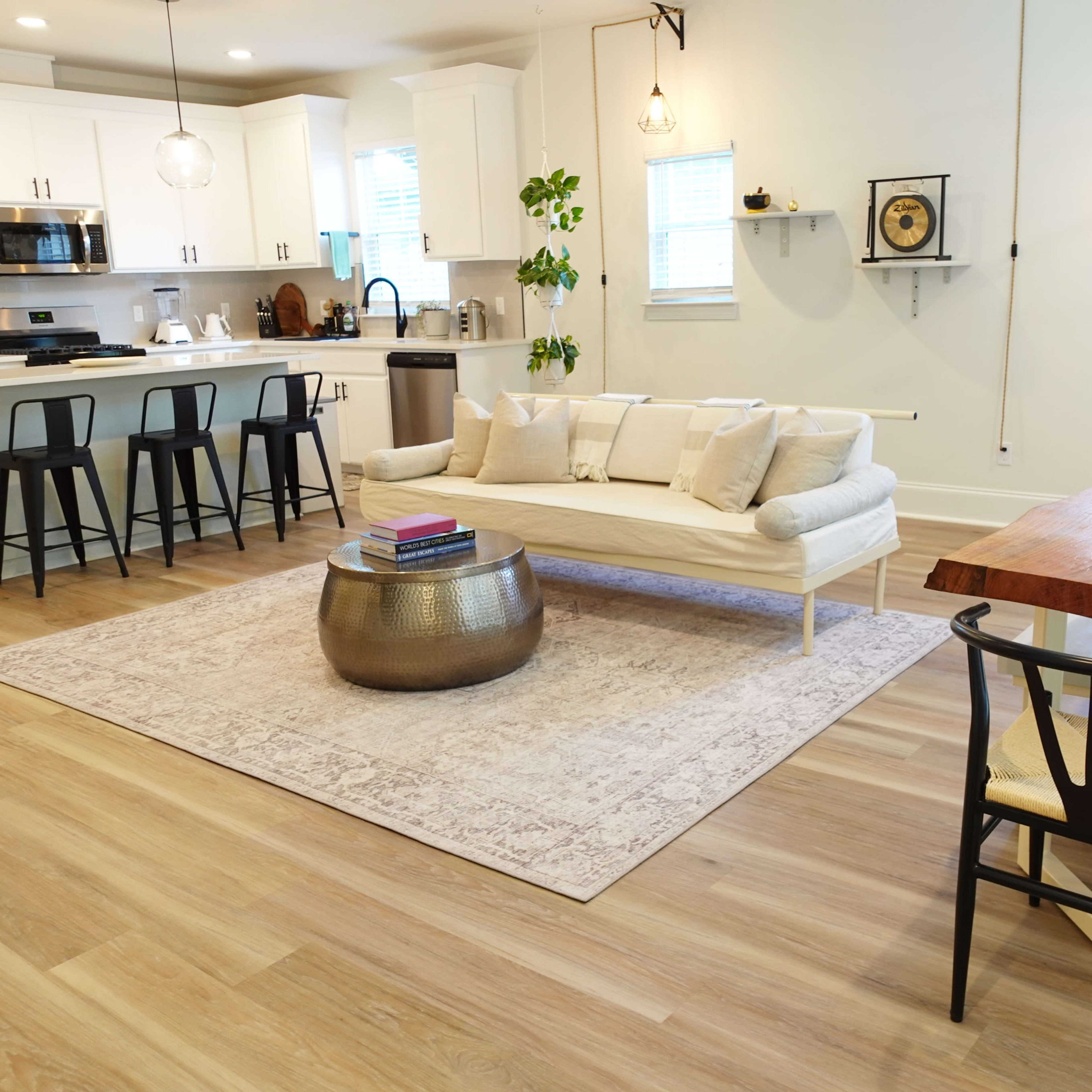 A modern living space with a white sofa, a wooden dining table, and a kitchen area equipped with appliances and bar stools.