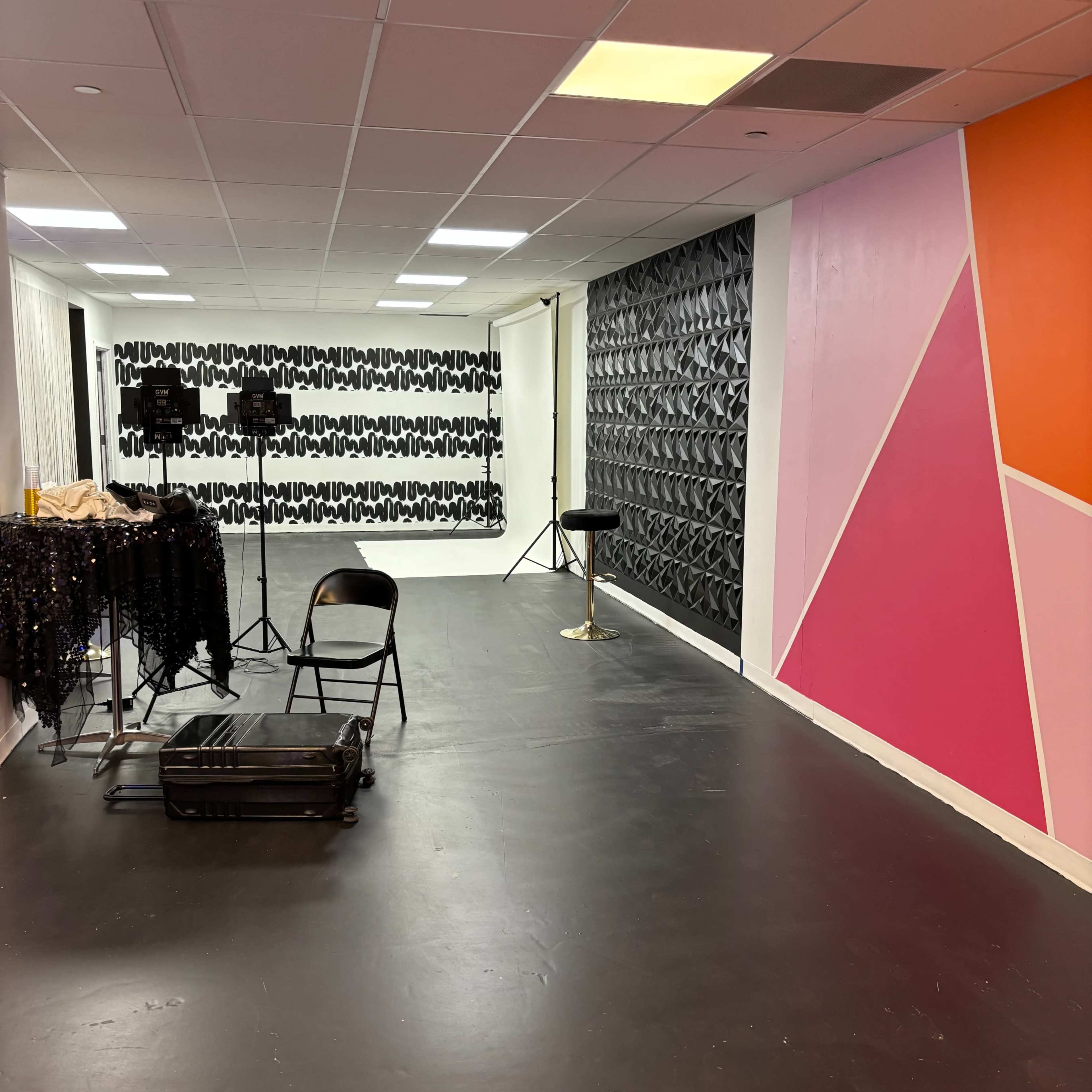 A spacious room with a black floor, featuring a patterned wall, a large solid-colored wall, and studio lighting equipment set up.