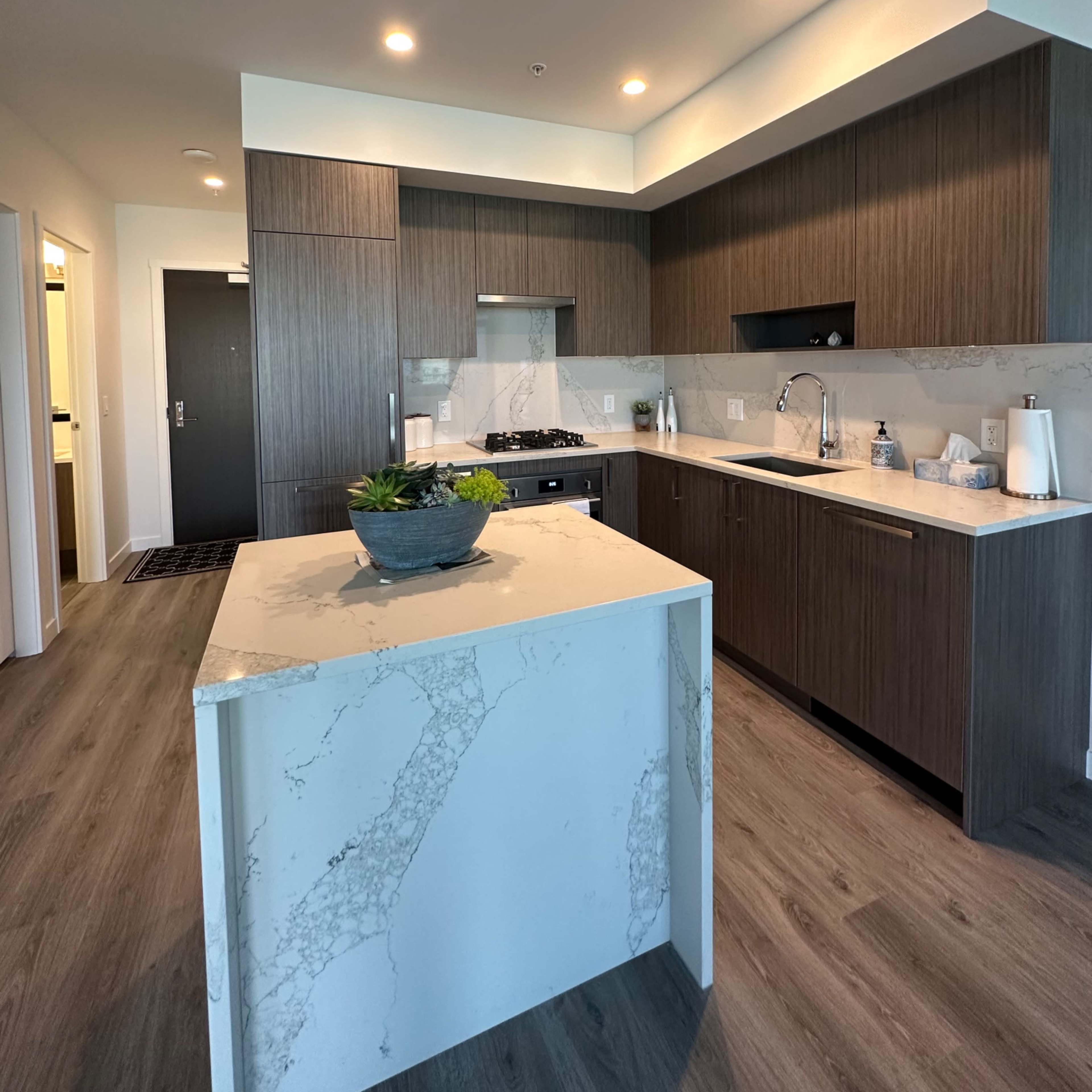 A modern kitchen with dark wood cabinetry, a marble countertop island, and stainless steel appliances.