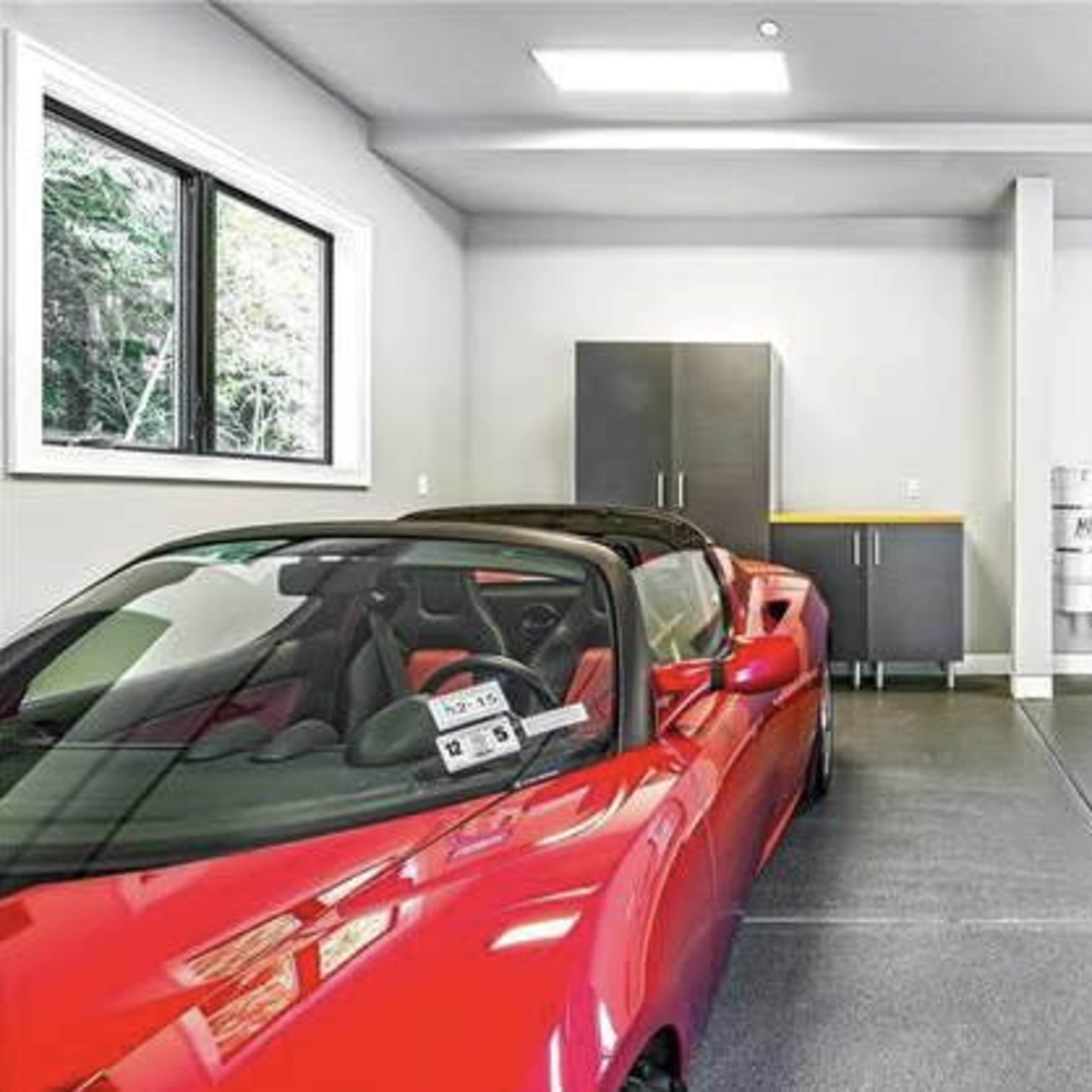 A red convertible sports car is parked in a modern garage featuring gray cabinets and large windows.