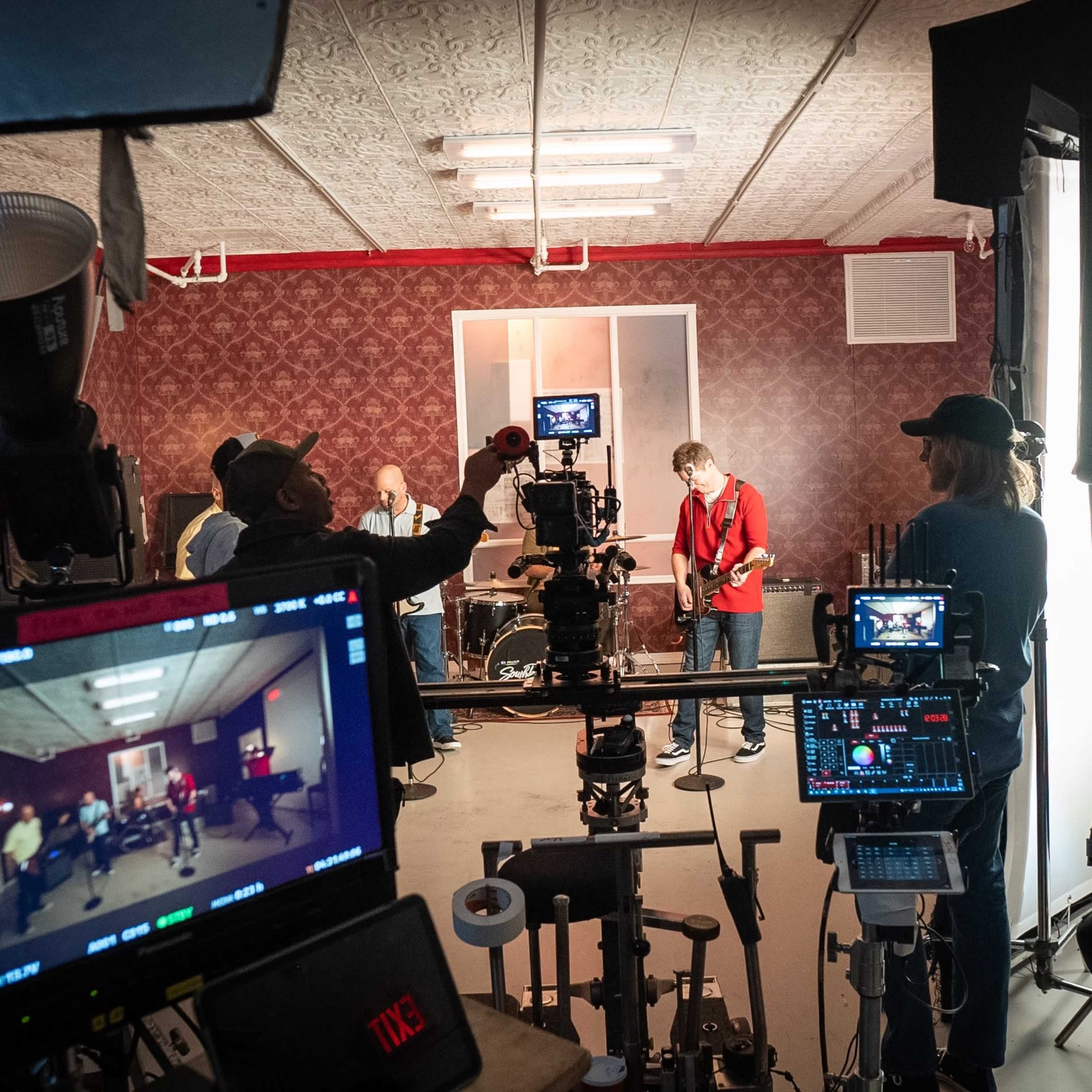 A music video is being filmed in a studio with musicians performing and crew members operating cameras and lights.