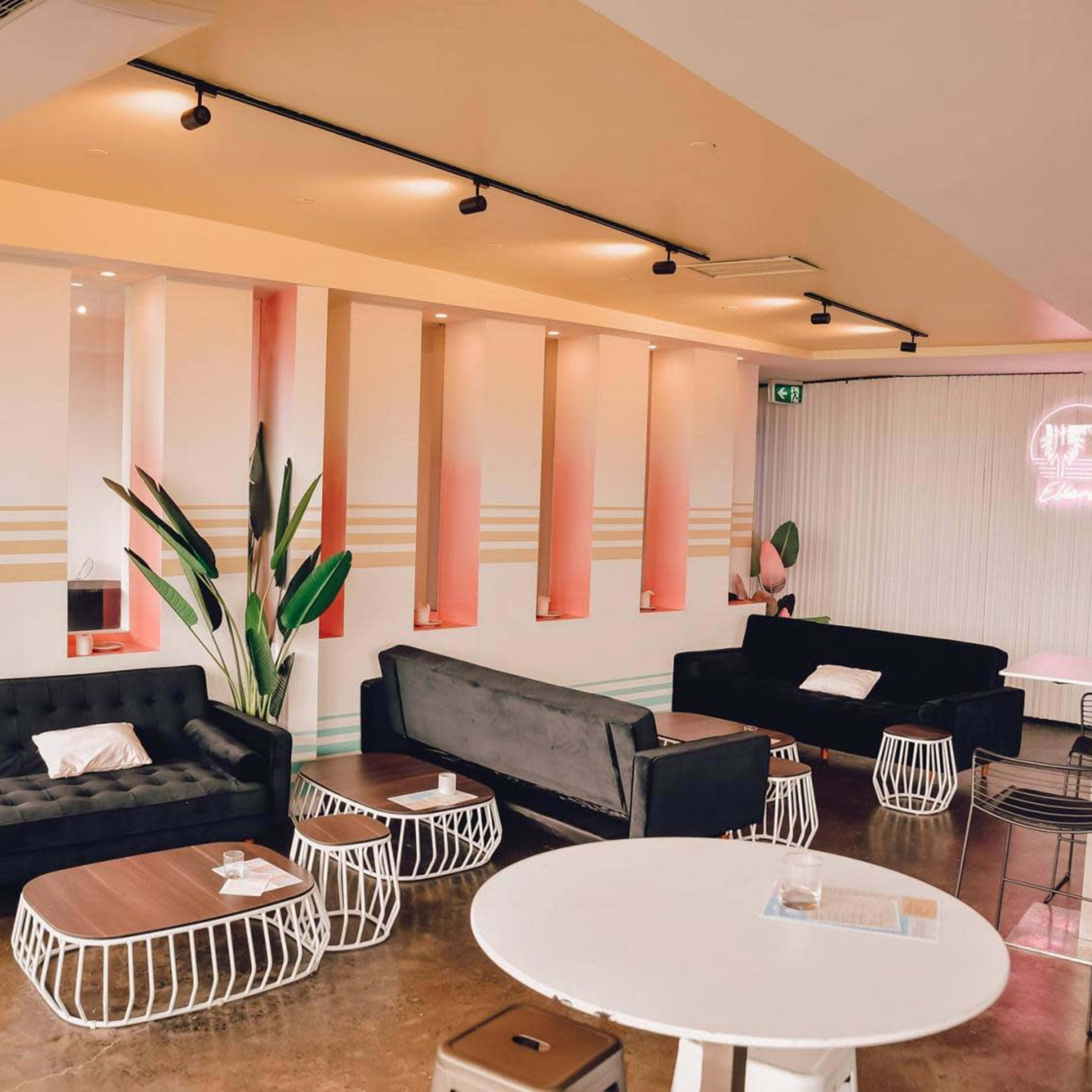 A modern café interior features black sofas, wooden tables, and decorative plants against a backdrop of pastel-colored walls.