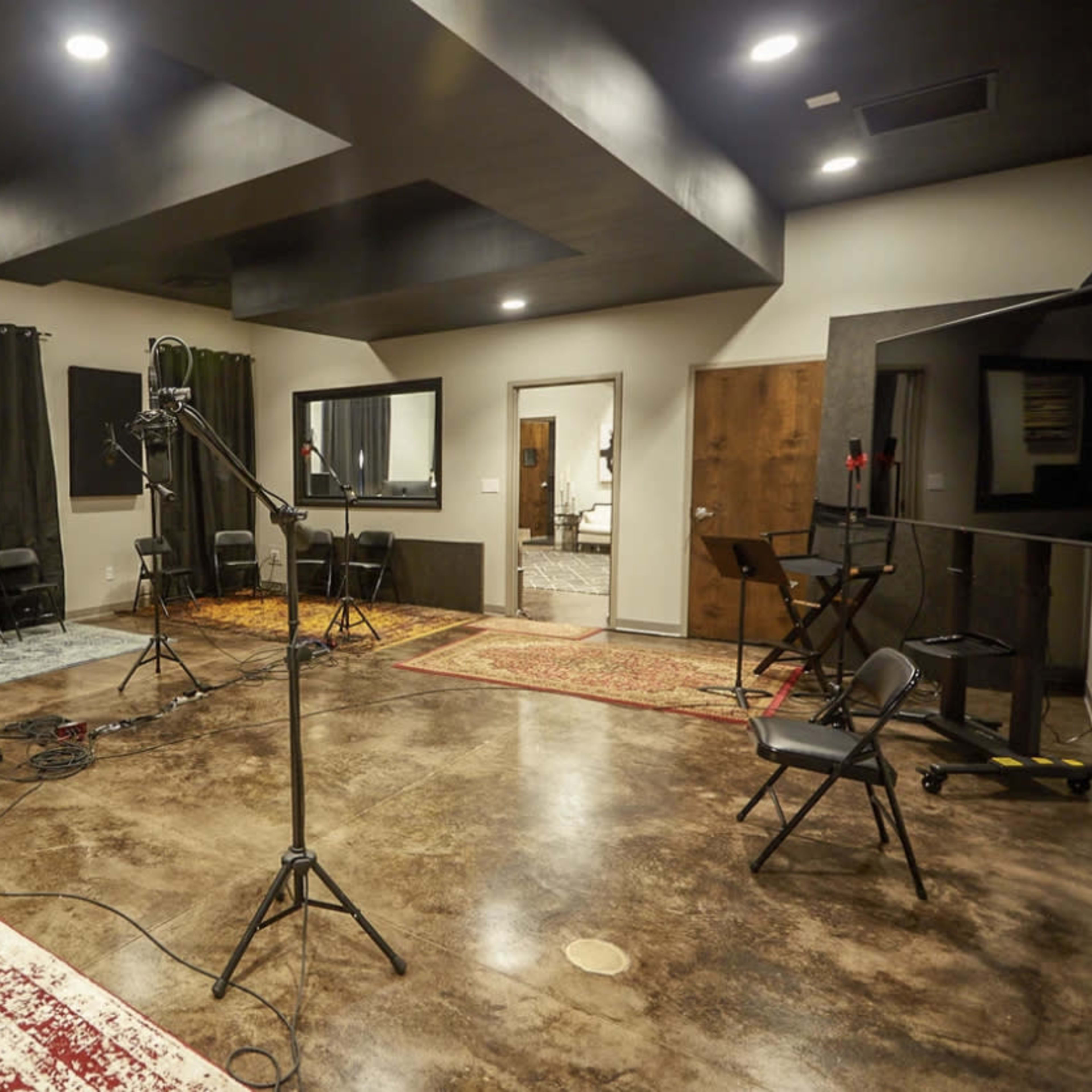 A recording studio with several chairs arranged around a central area, soundproof panels on the walls, and microphones on stands.