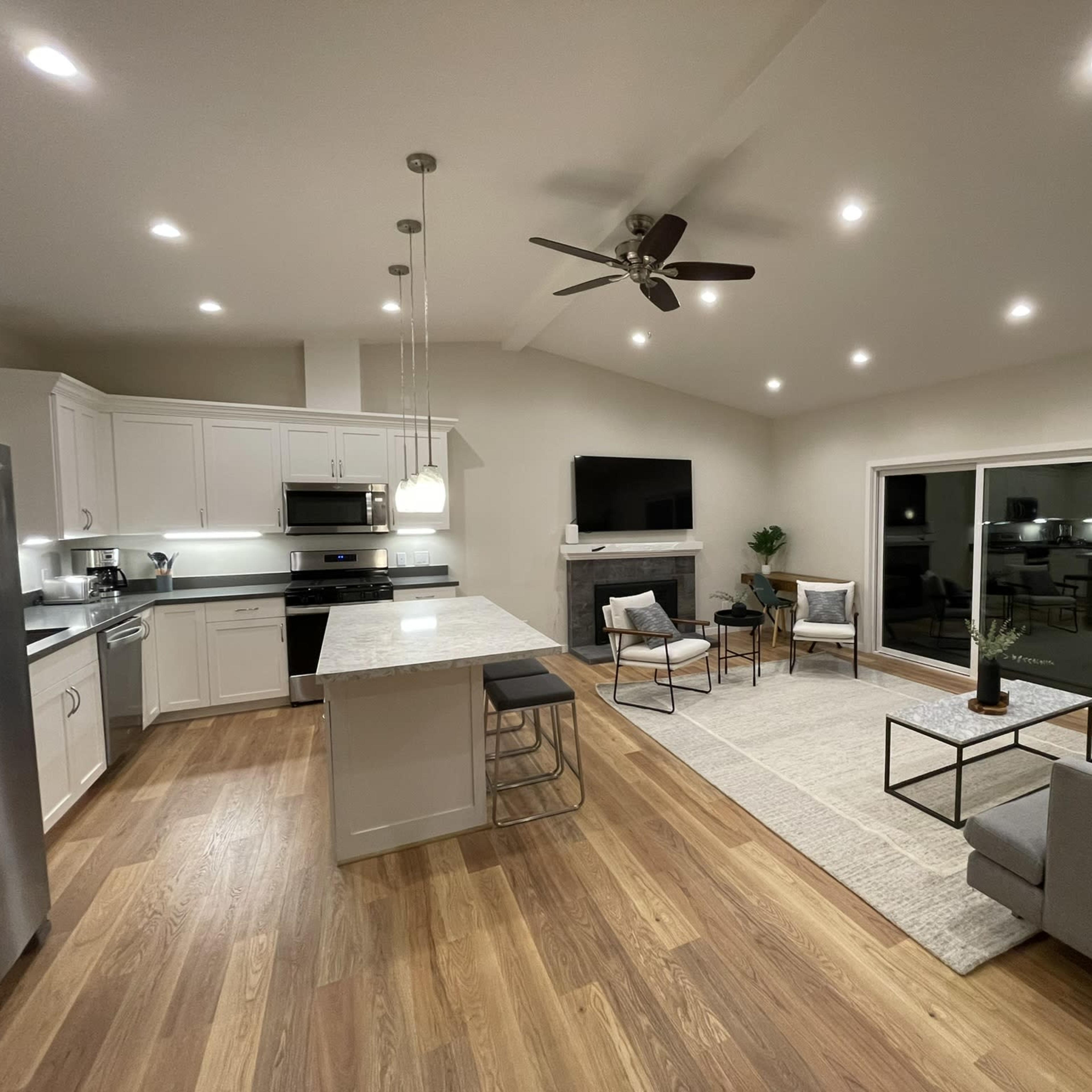 A modern open-concept living space with a kitchen, dining area, and seating area featuring contemporary furniture and a large window.