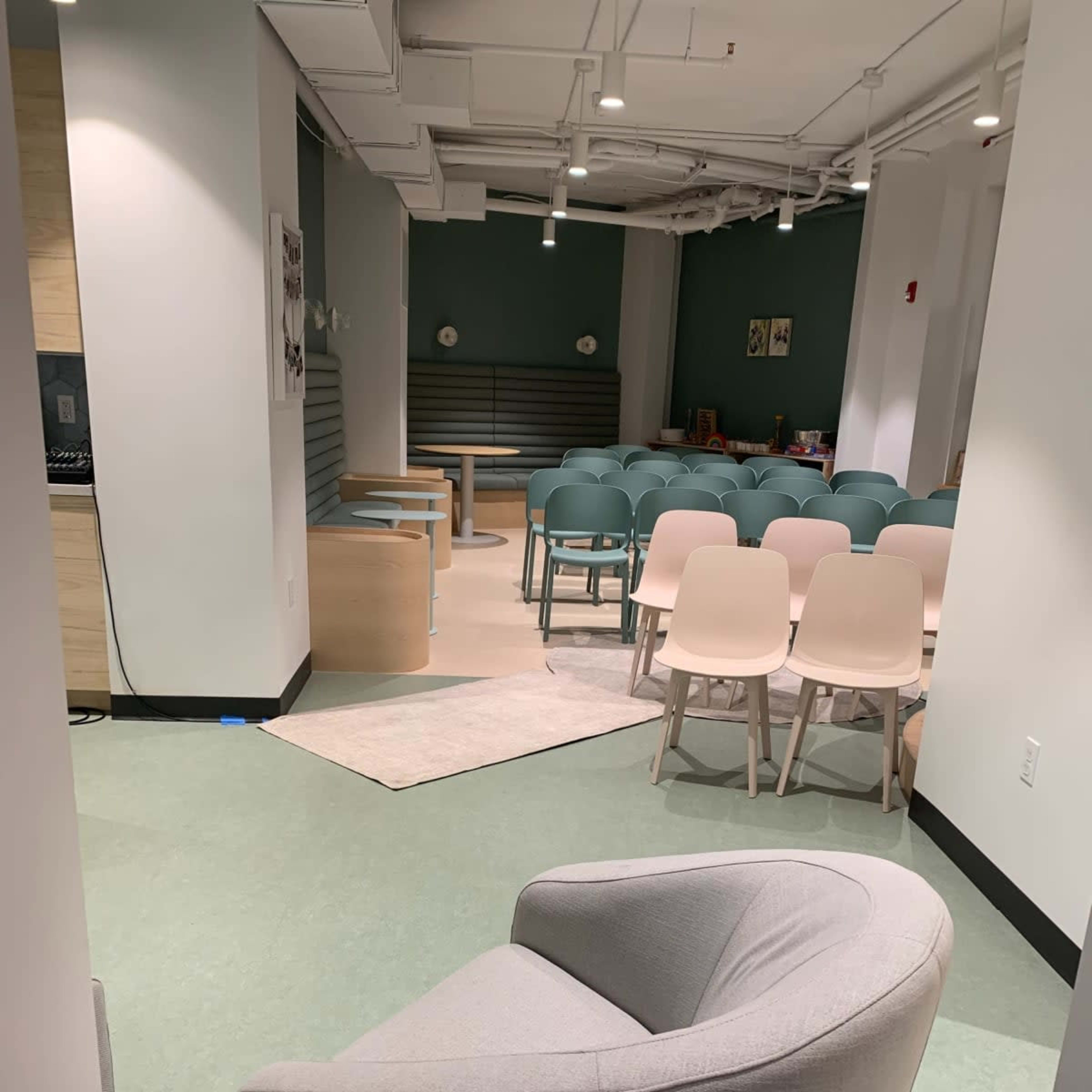 A seating area with a grey armchair and a semi-circle of light-colored chairs arranged for an event in a modern room.