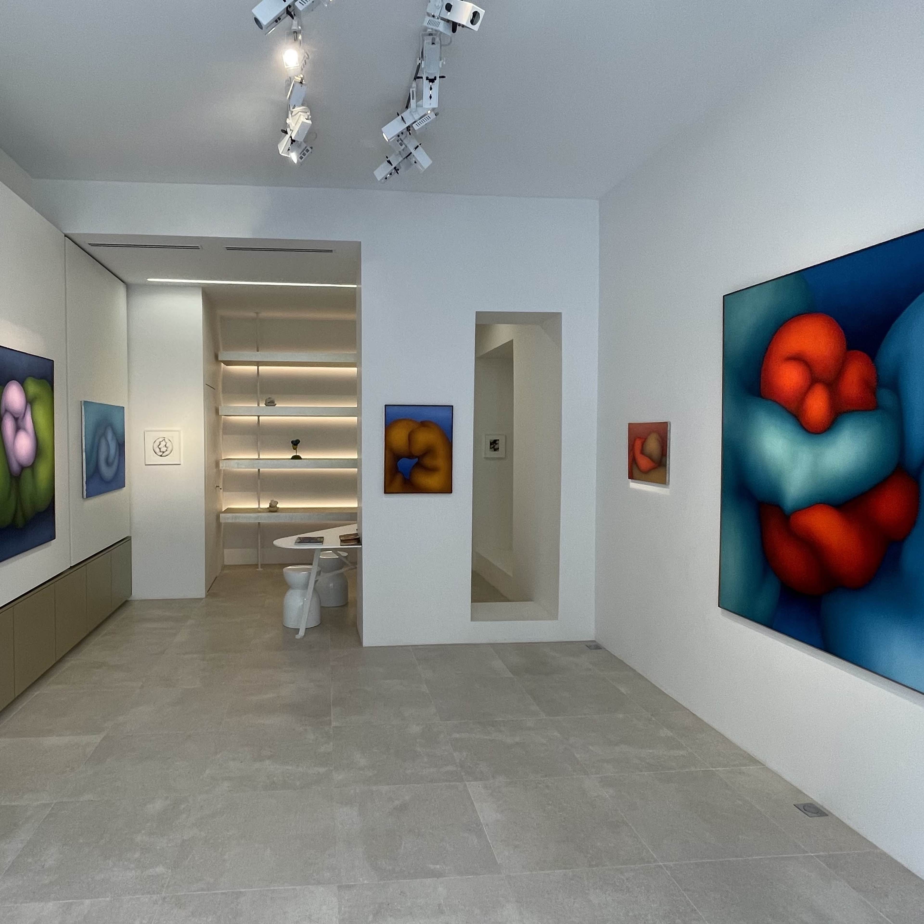 A modern art gallery with abstract paintings on the walls and a minimalist exhibition space featuring a table and a set of stools.
