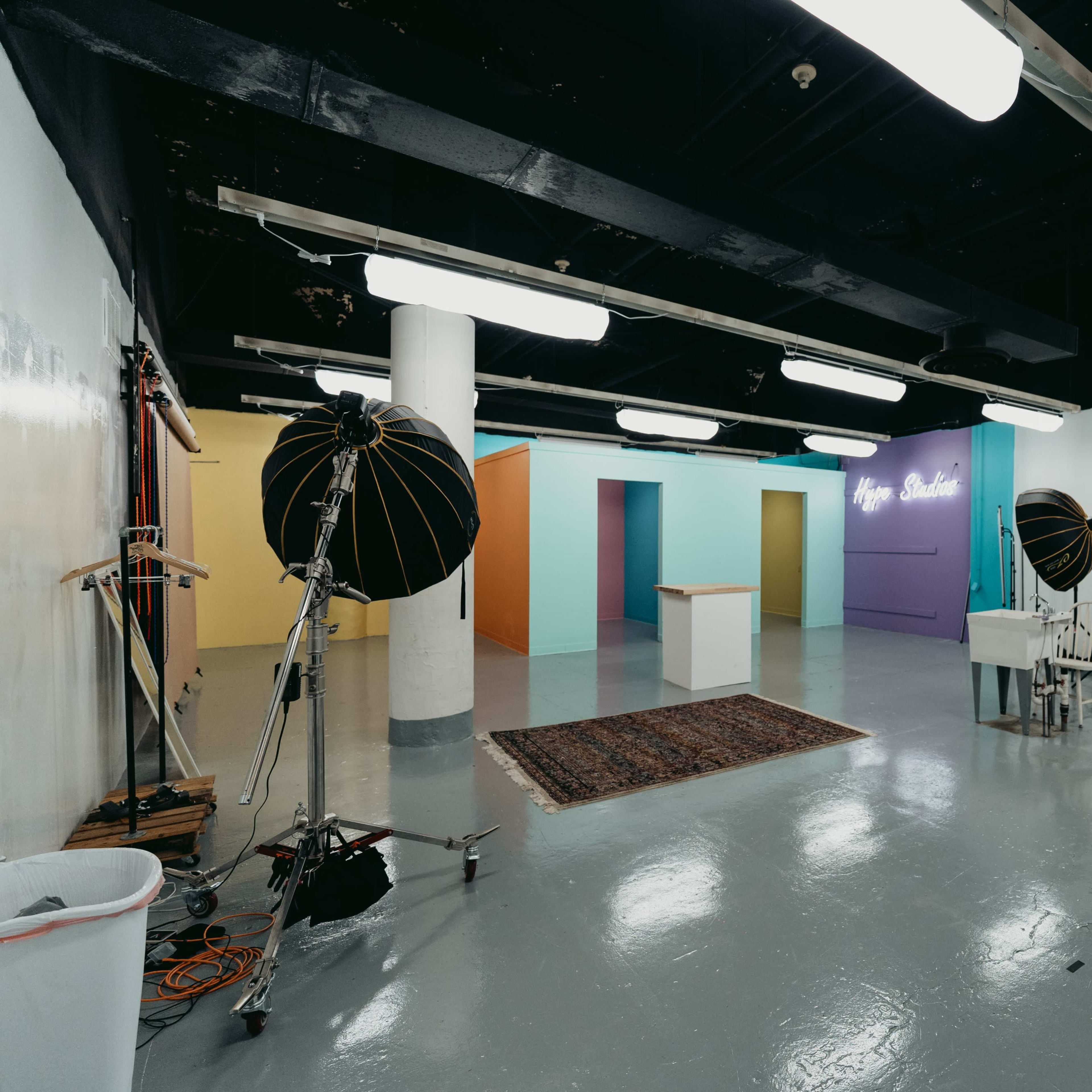 A spacious photo studio with bright colored walls, a white backdrop, lighting equipment, and various props arranged throughout the room.