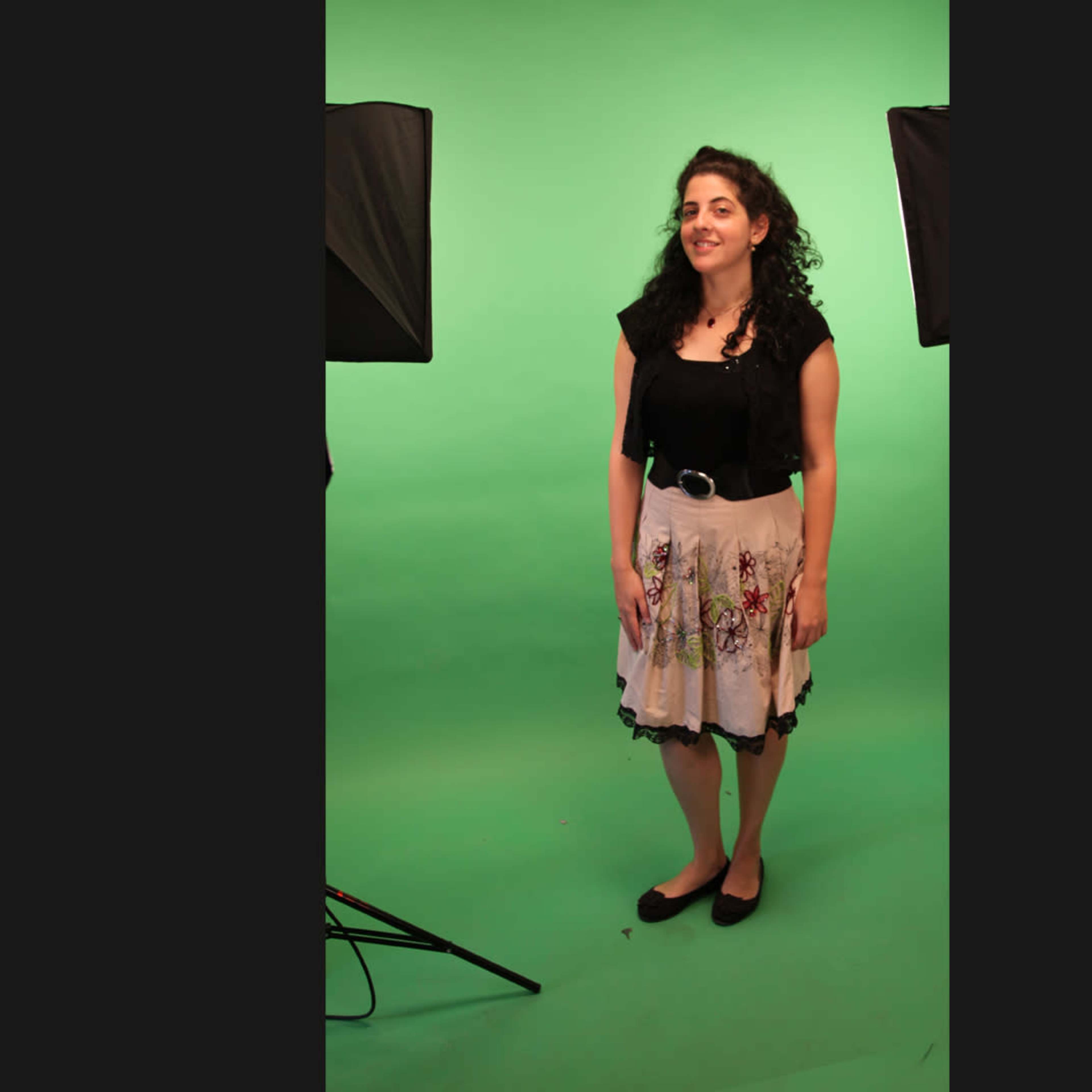 A woman stands on a green backdrop with studio lights positioned on either side.