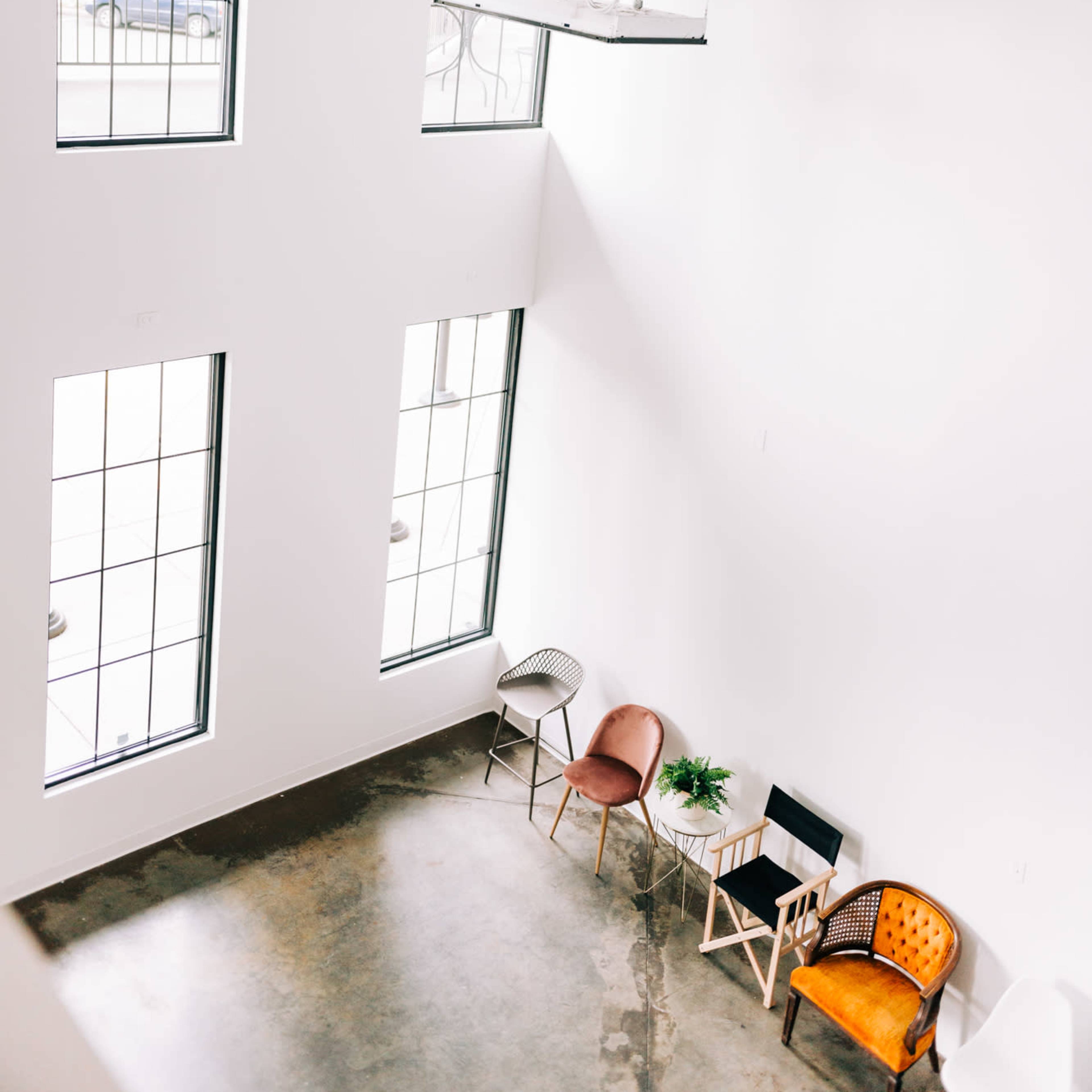 A spacious, minimalist room with large windows and a few chairs arranged near a small table in one corner.