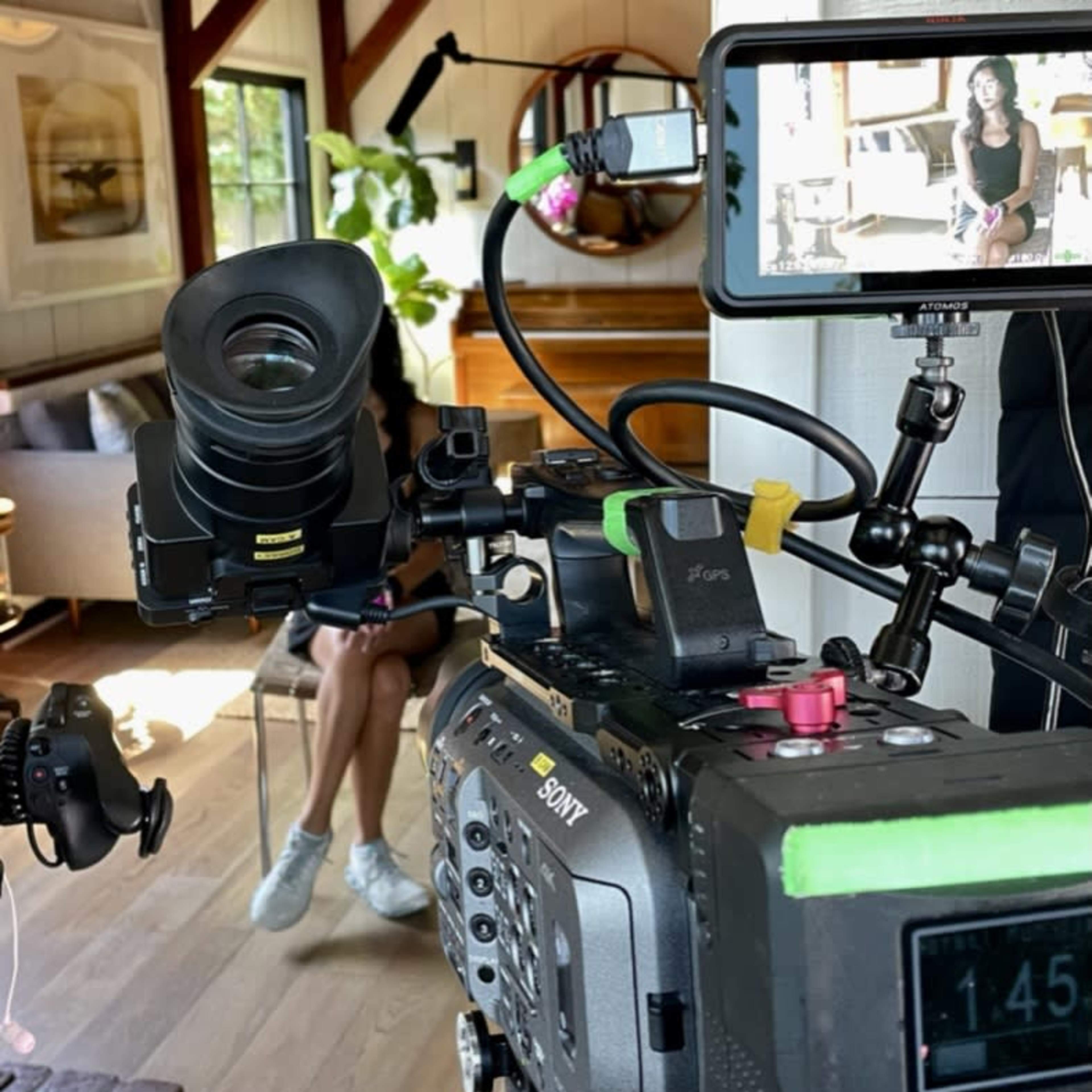 A camera setup focused on a woman sitting in a chair, with the camera's monitor displaying her image.