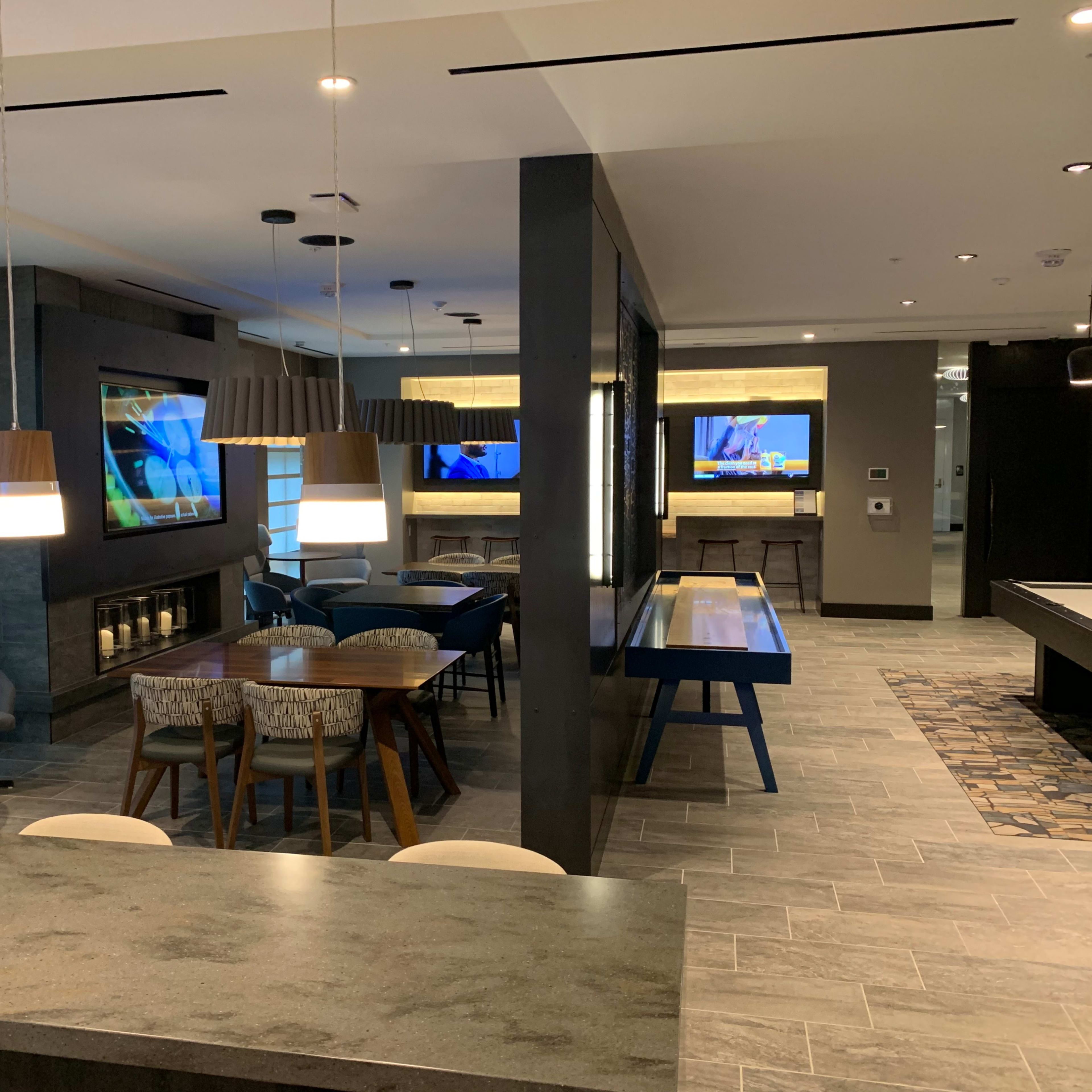A modern communal space with couches, tables, and large televisions mounted on the walls.
