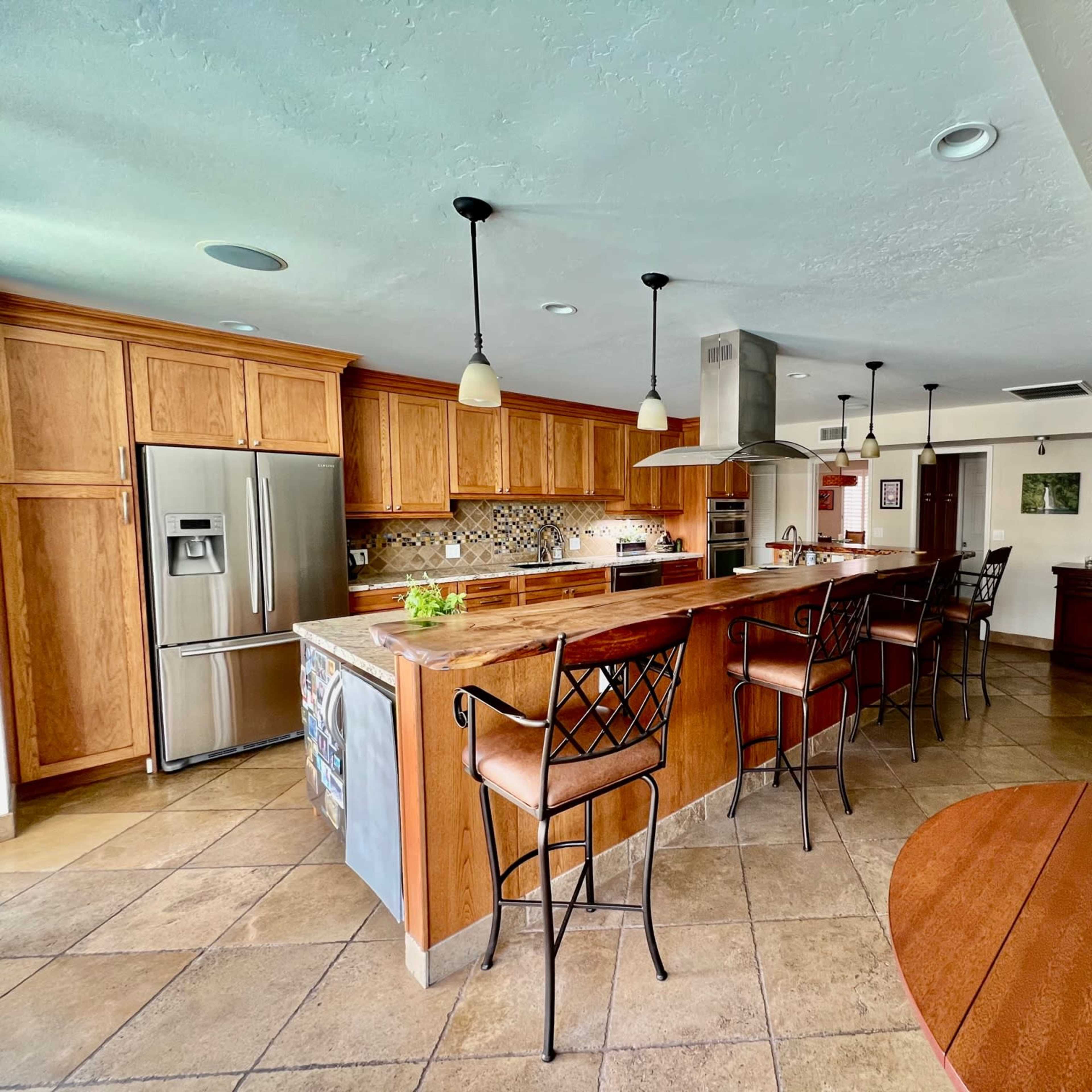 The kitchen features wooden cabinetry, a large island with bar seating, stainless steel appliances, and a dining area with a round table.
