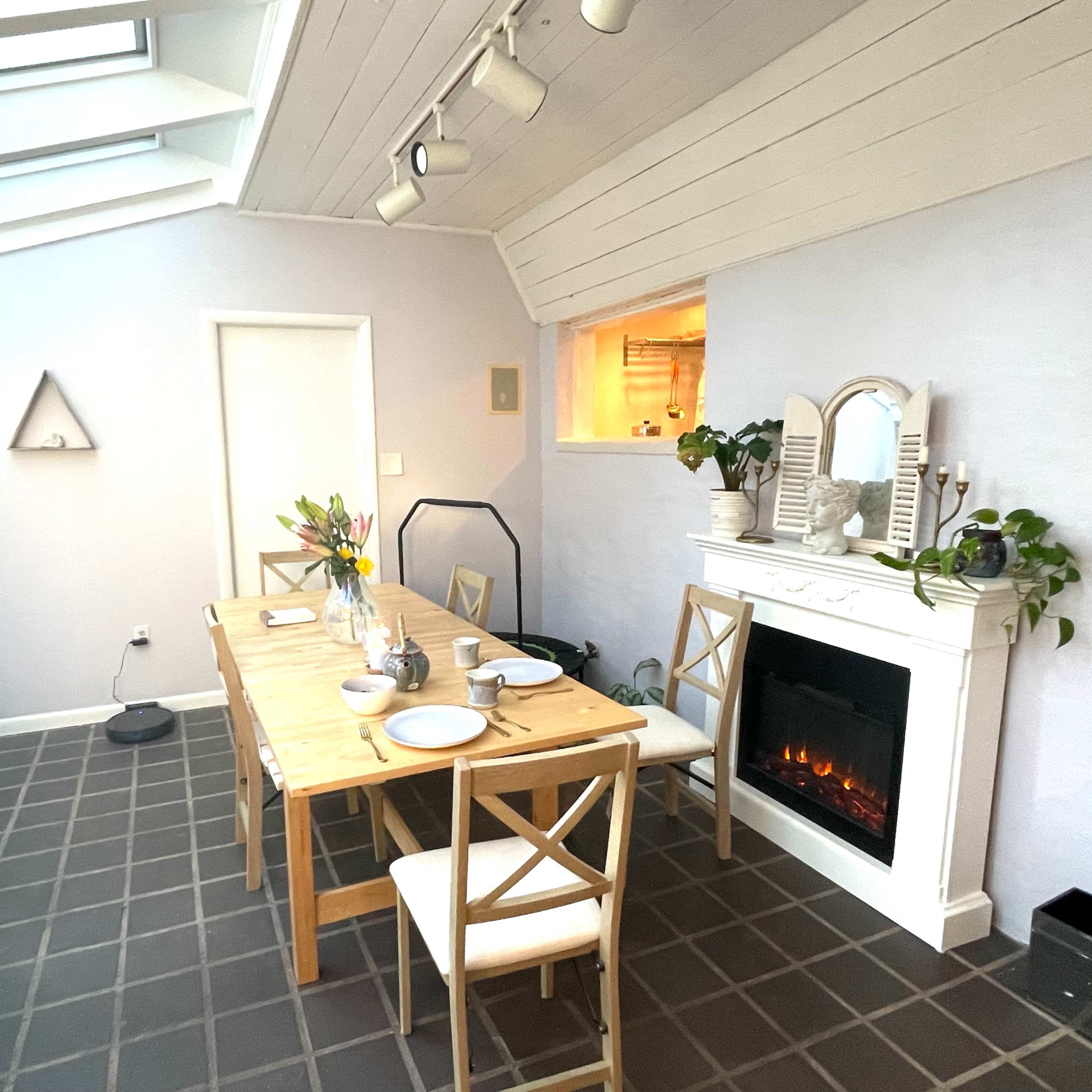 A dining area with a wooden table set for a meal, a modern fireplace, and a large skylight above.