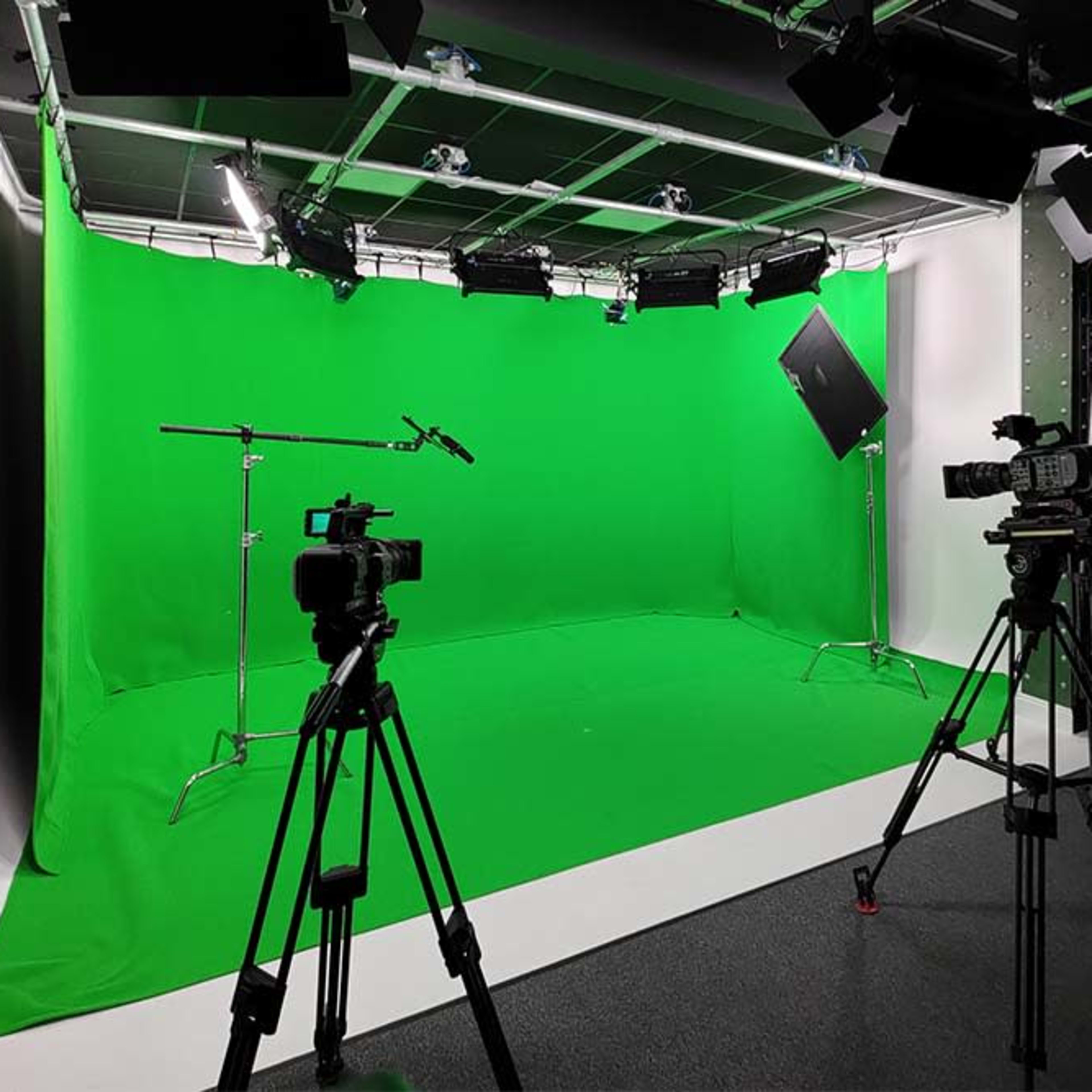 A green screen studio setup with two video cameras, lights, and equipment stands arranged around a bright green backdrop.