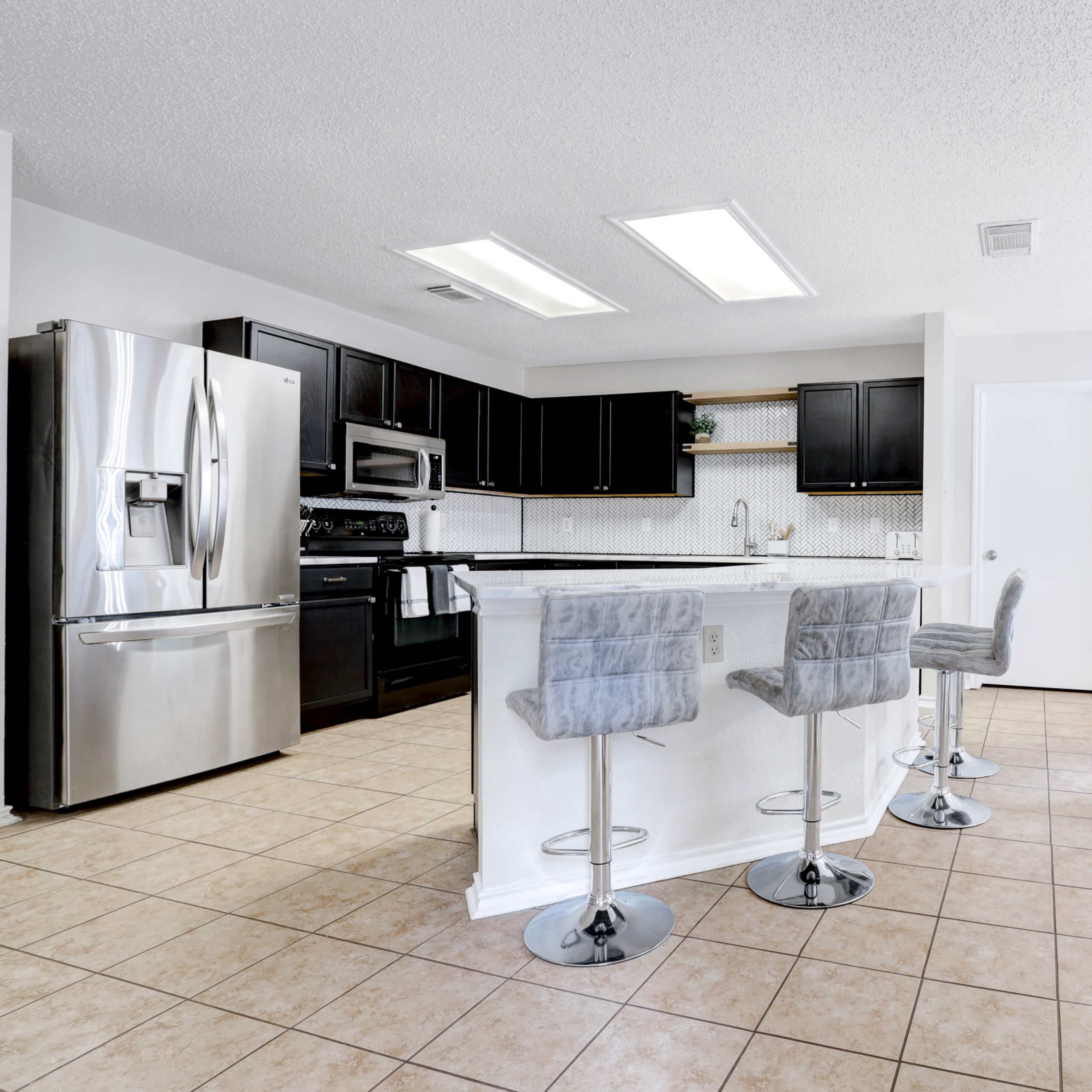 A modern kitchen features stainless steel appliances, dark cabinetry, and a central island with bar stools.