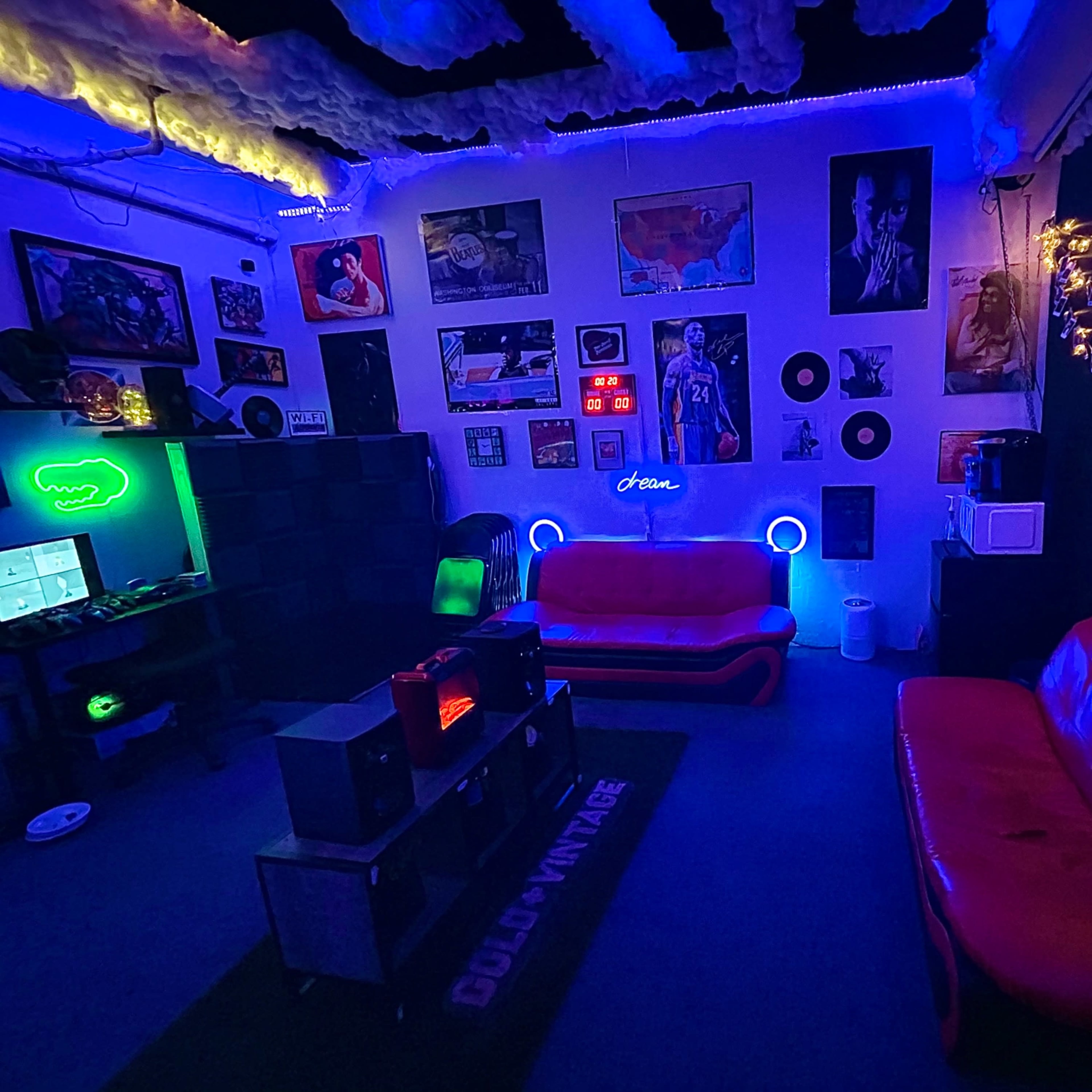 A dimly lit room with red couches, colorful lighting, and various posters and decorations on the walls.