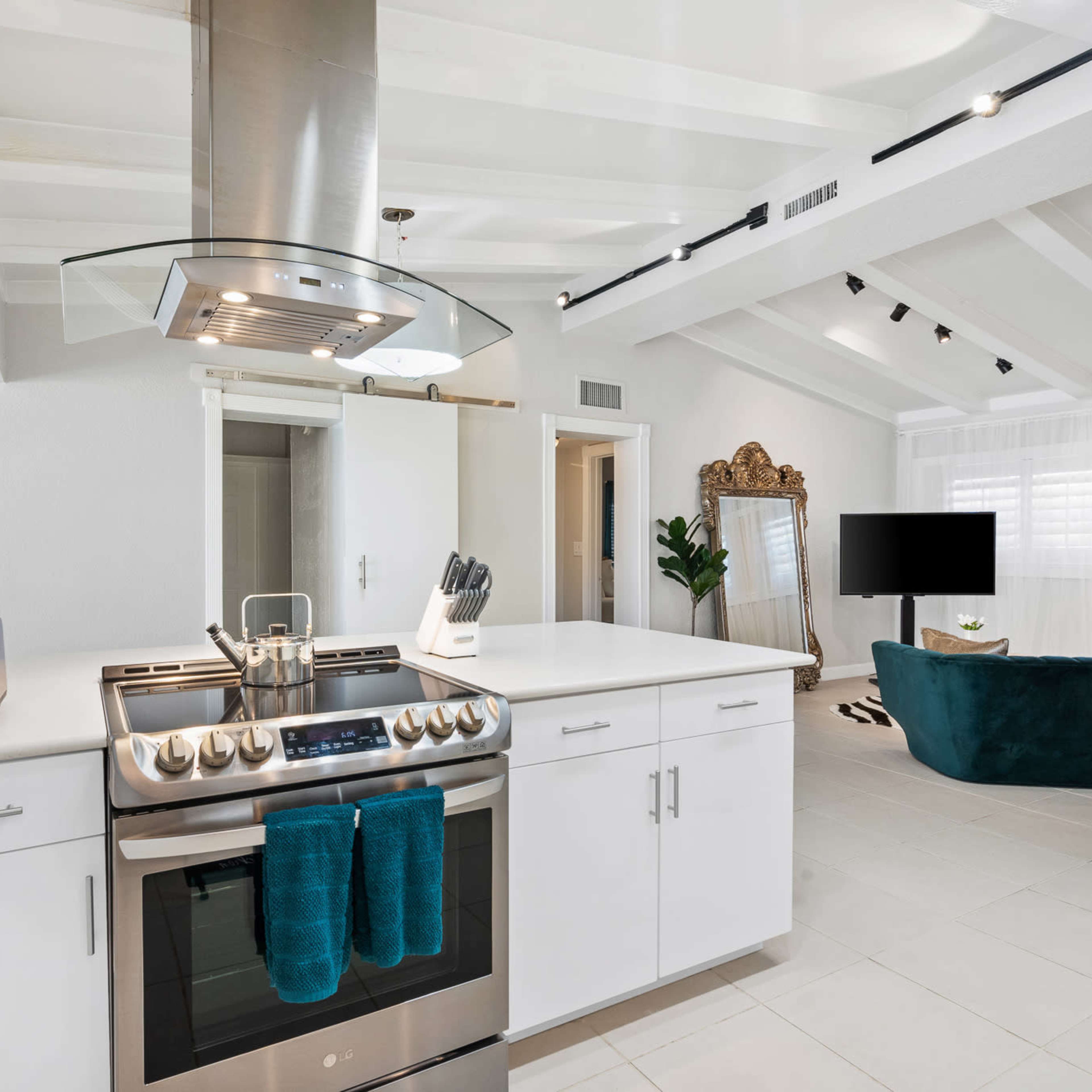 A modern kitchen with a stainless steel stove, white cabinets, and an open layout leading to a living area with a green sofa.