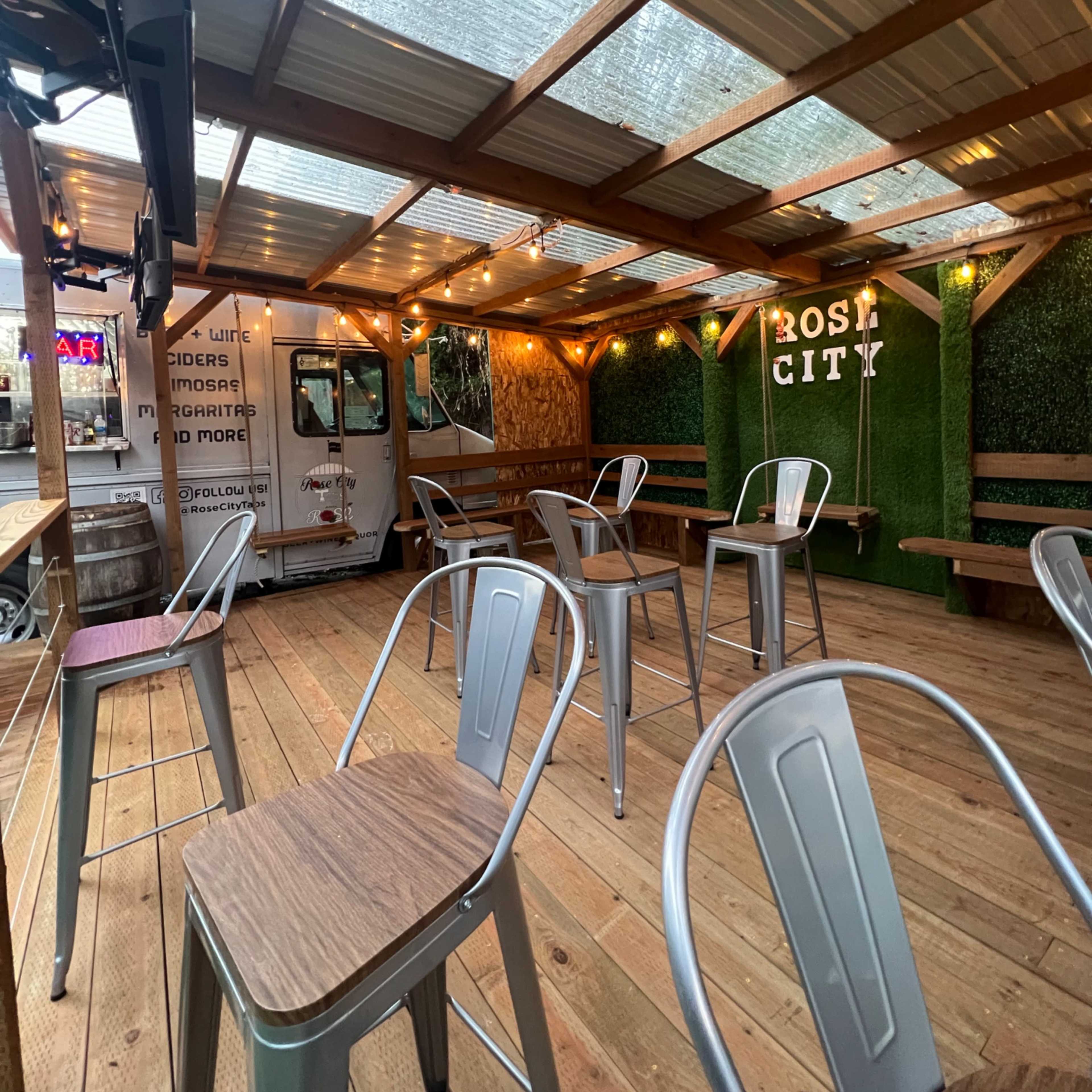An outdoor seating area with metal chairs, wooden tables, and string lights under a covered roof.