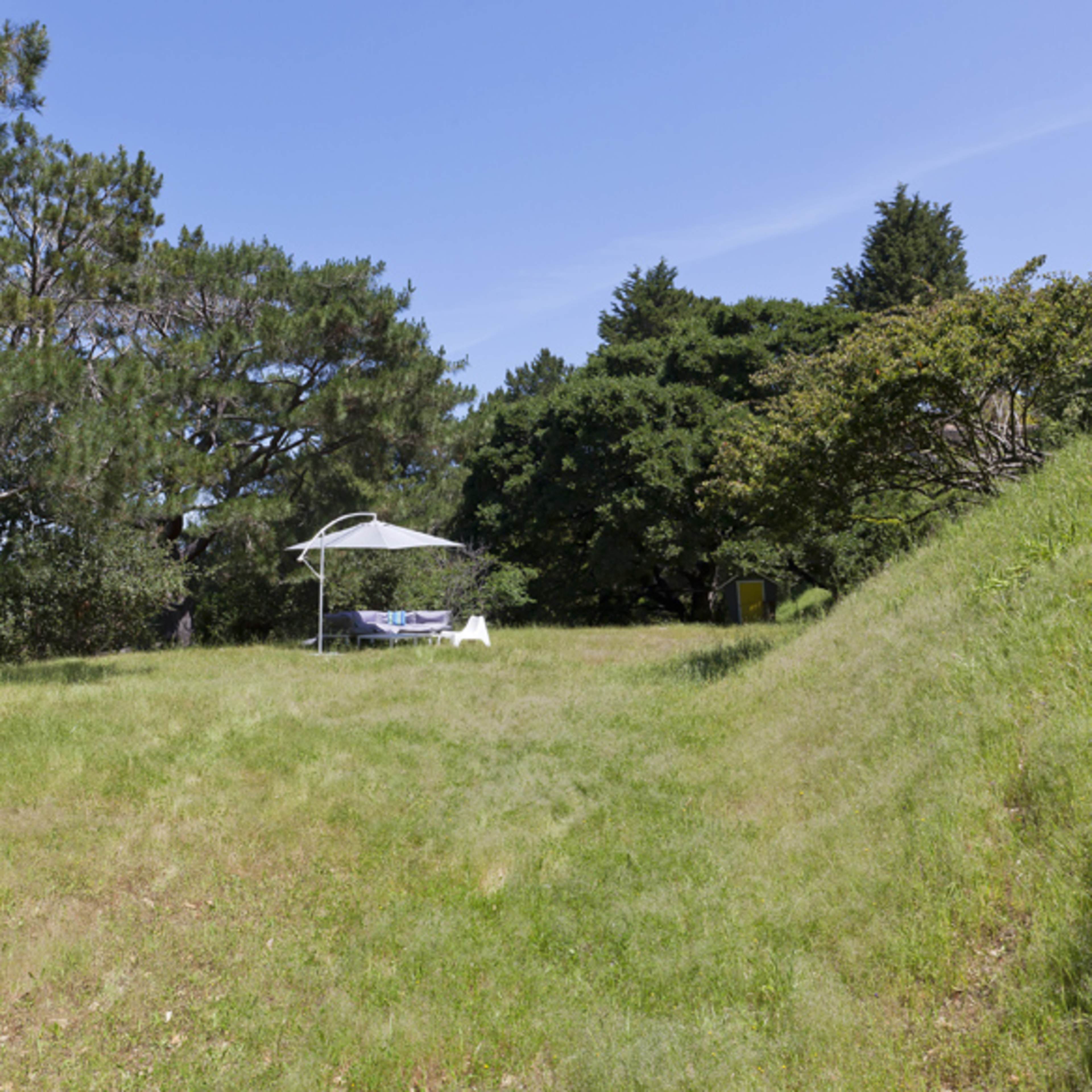 A grassy area is set up with a table and an umbrella beneath some trees.