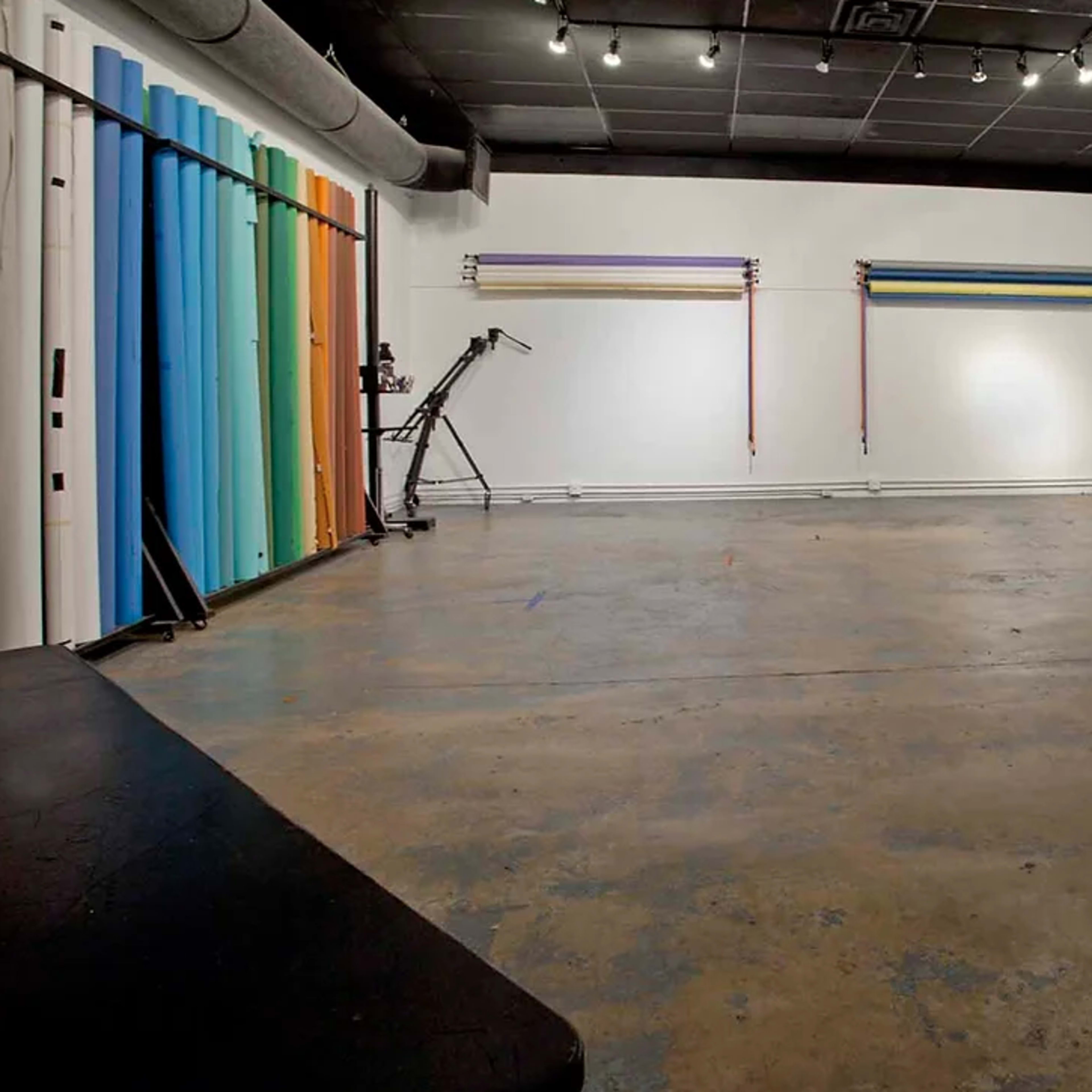 A spacious photography studio with colored backdrops, lighting equipment, and a concrete floor.
