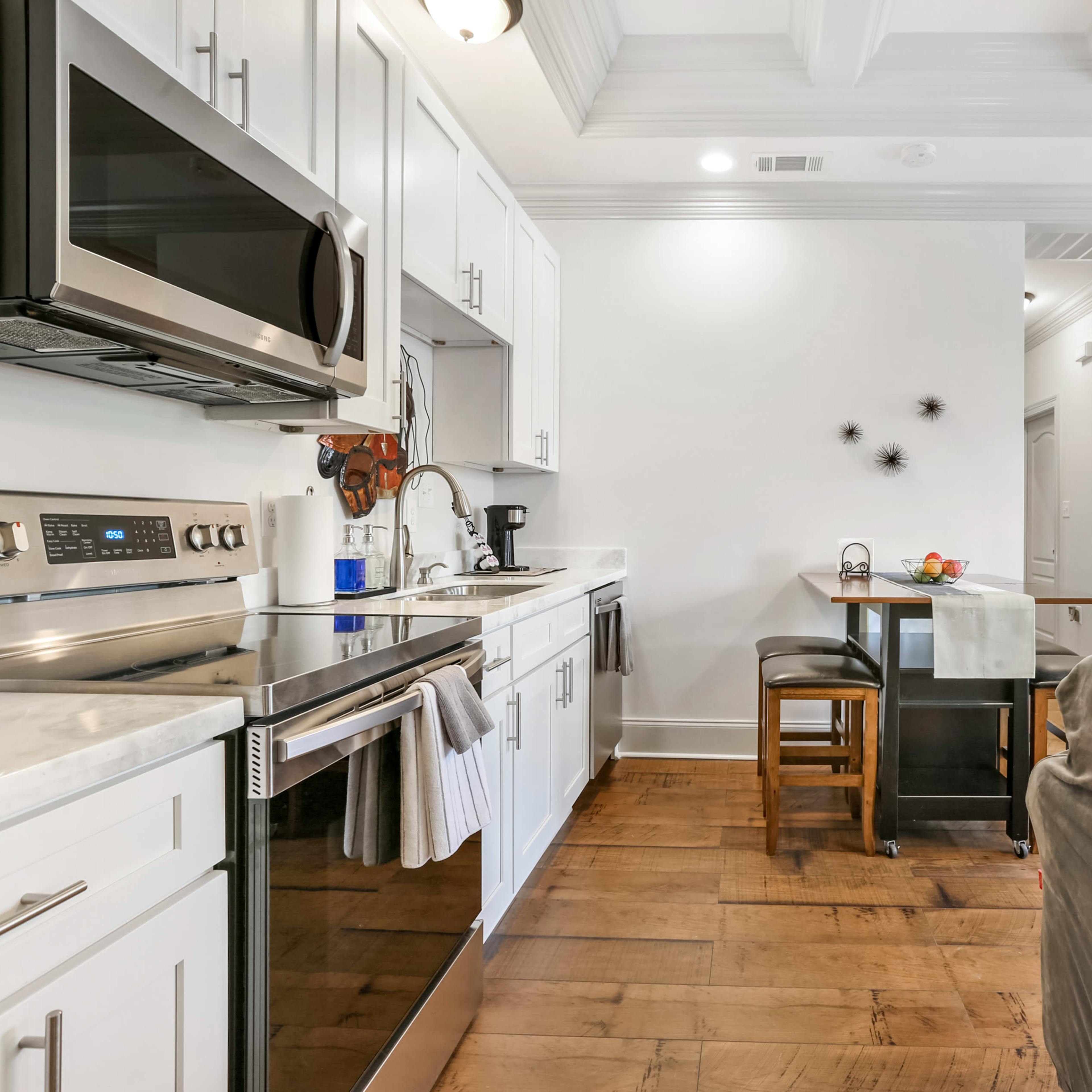 A modern kitchen with stainless steel appliances, white cabinetry, and a small dining area with two barstools.