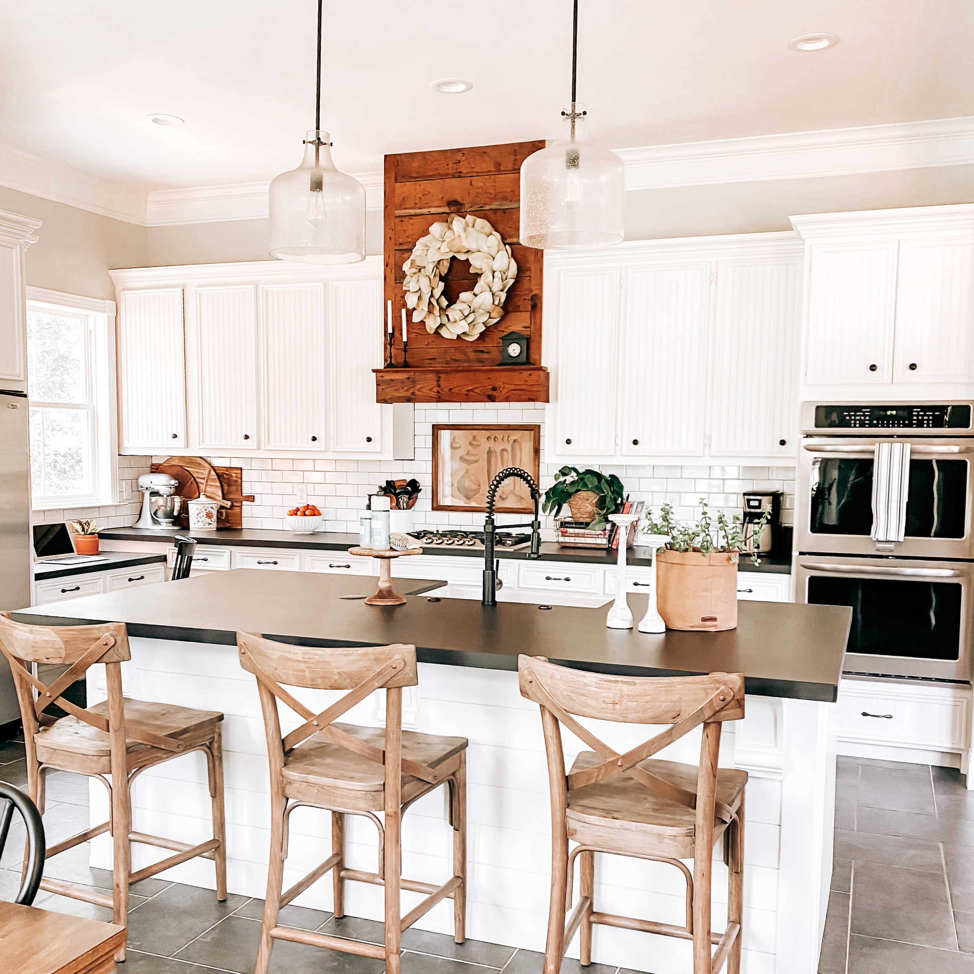 A modern kitchen features white cabinetry, a dark countertop, wooden bar stools, and pendant lighting over an island with decorative elements.