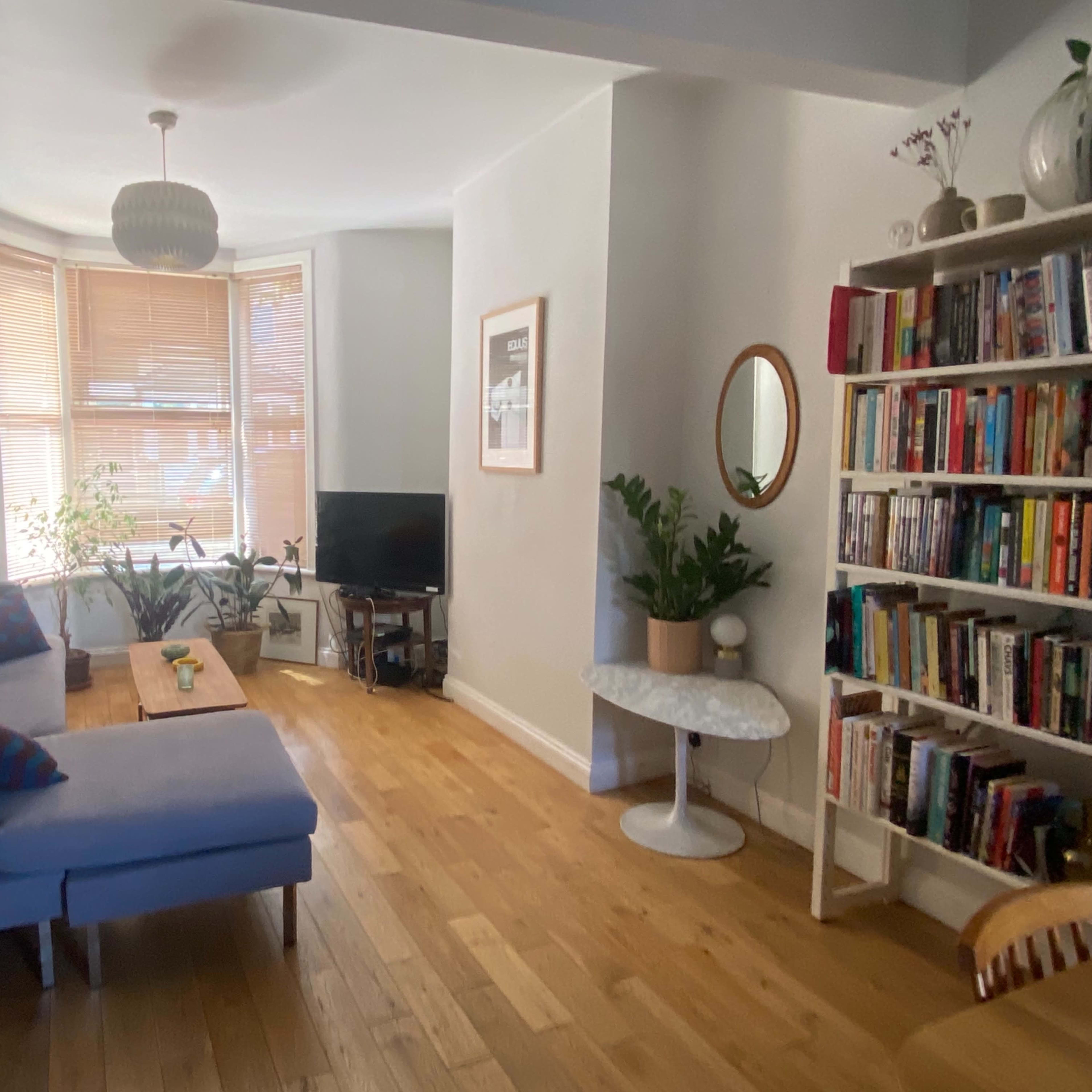 A cozy living room with a gray sectional sofa, a wooden coffee table, a television, and a bookshelf filled with books, along with plants by the window.