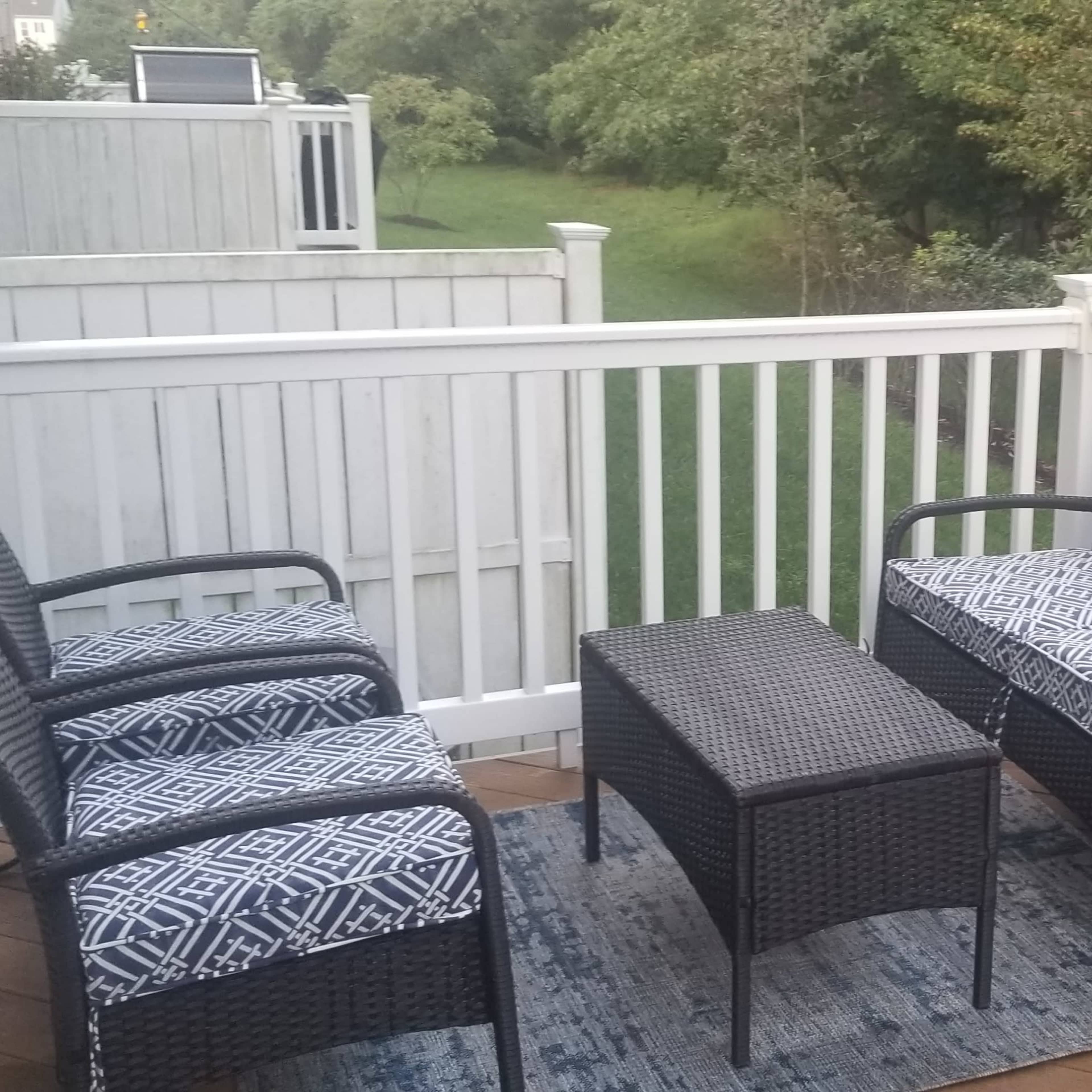 A small outdoor seating area with two wicker chairs and a coffee table on a wooden deck, surrounded by greenery.