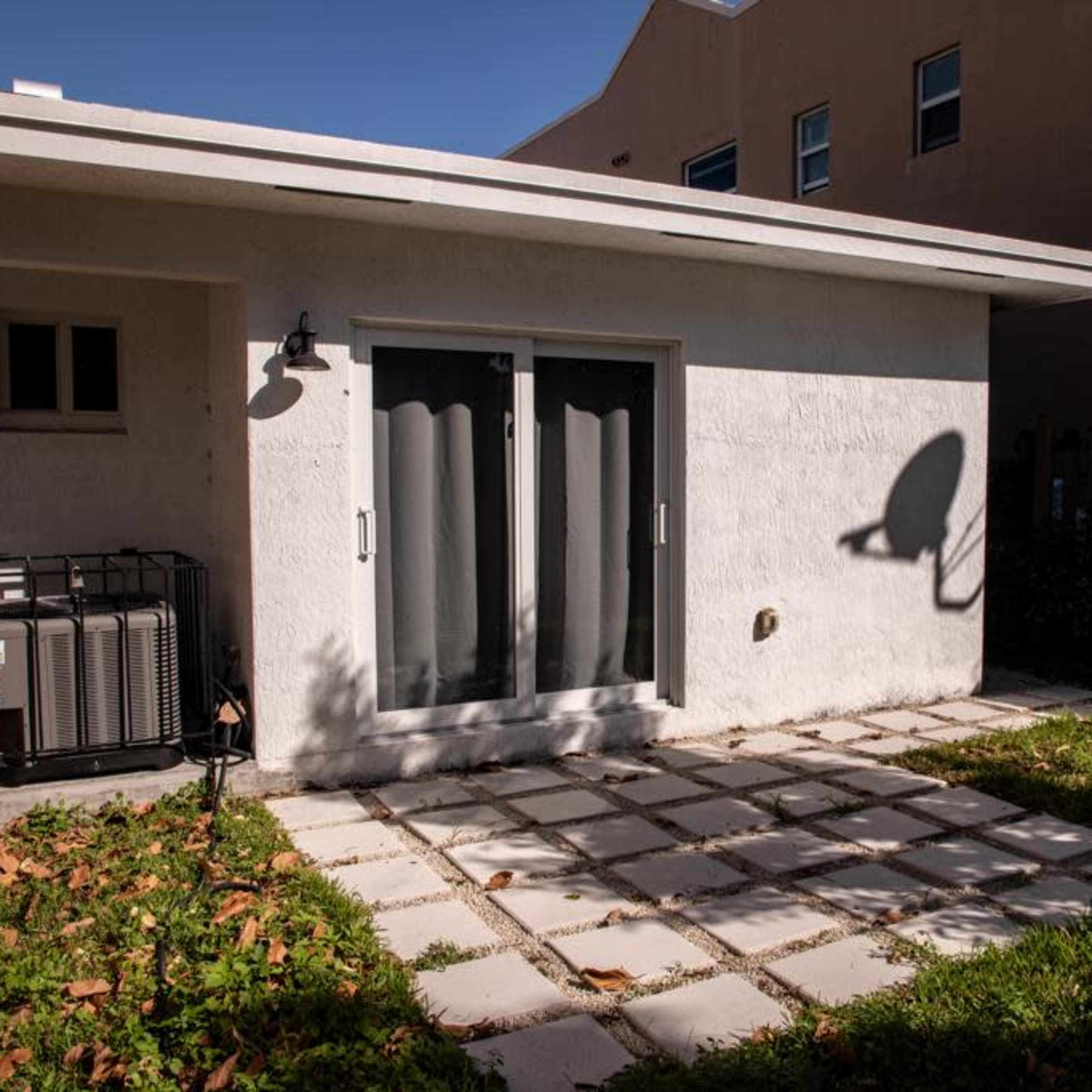 A small patio area features a concrete slab pathway leading to a set of sliding glass doors, with an air conditioning unit and a satellite dish present.